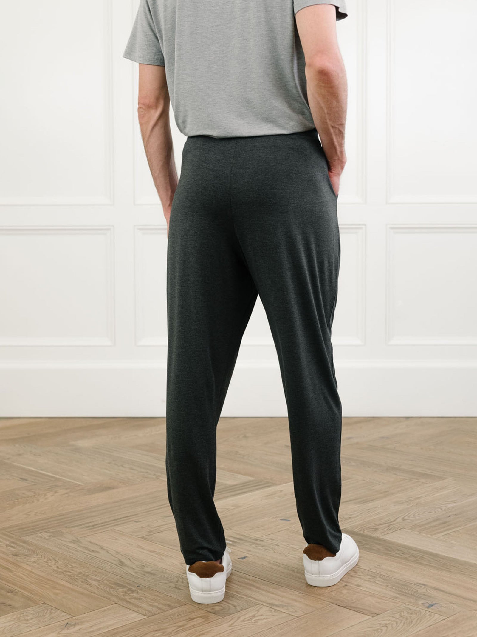 A person stands with their back to the camera, wearing a Cozy Earth Men's Stretch-Knit Long Sleeve Bamboo Pajama Set. The background features white panel walls and a wooden floor. 