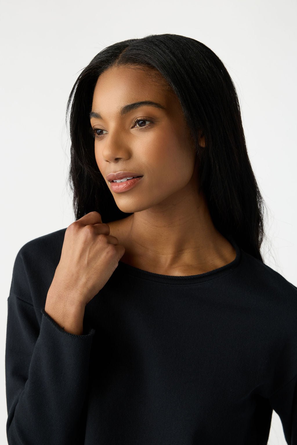 A woman with long dark hair looks to the side, wearing Cozy Earth's Women's Chelsea Set in black. She holds one hand near her shoulder, exuding a calm and thoughtful expression against a plain background. 