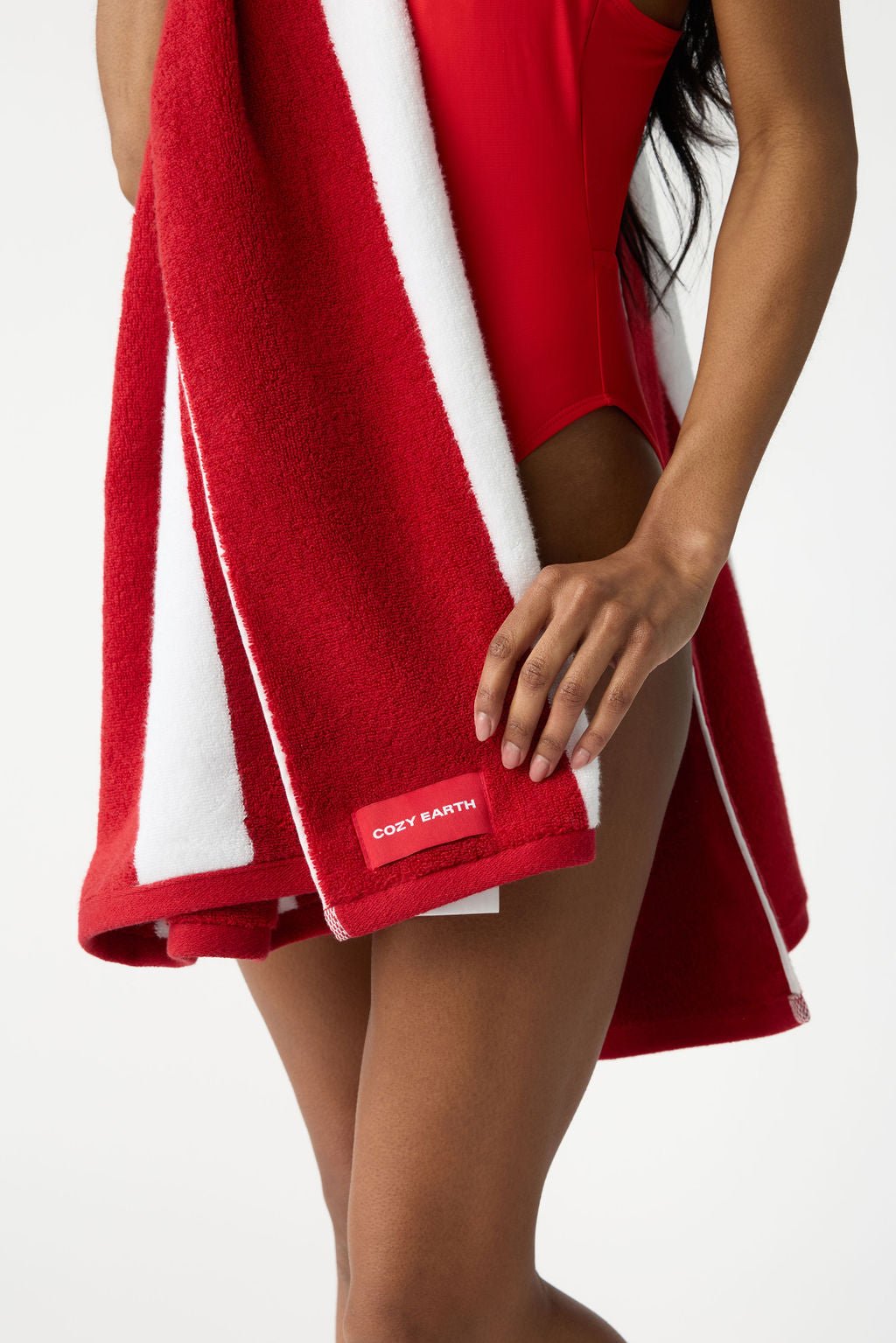 A person in a red swimsuit is holding the "Cozy Earth Classic Stripe Resort Towel" in red and white, visible from the neck down. 