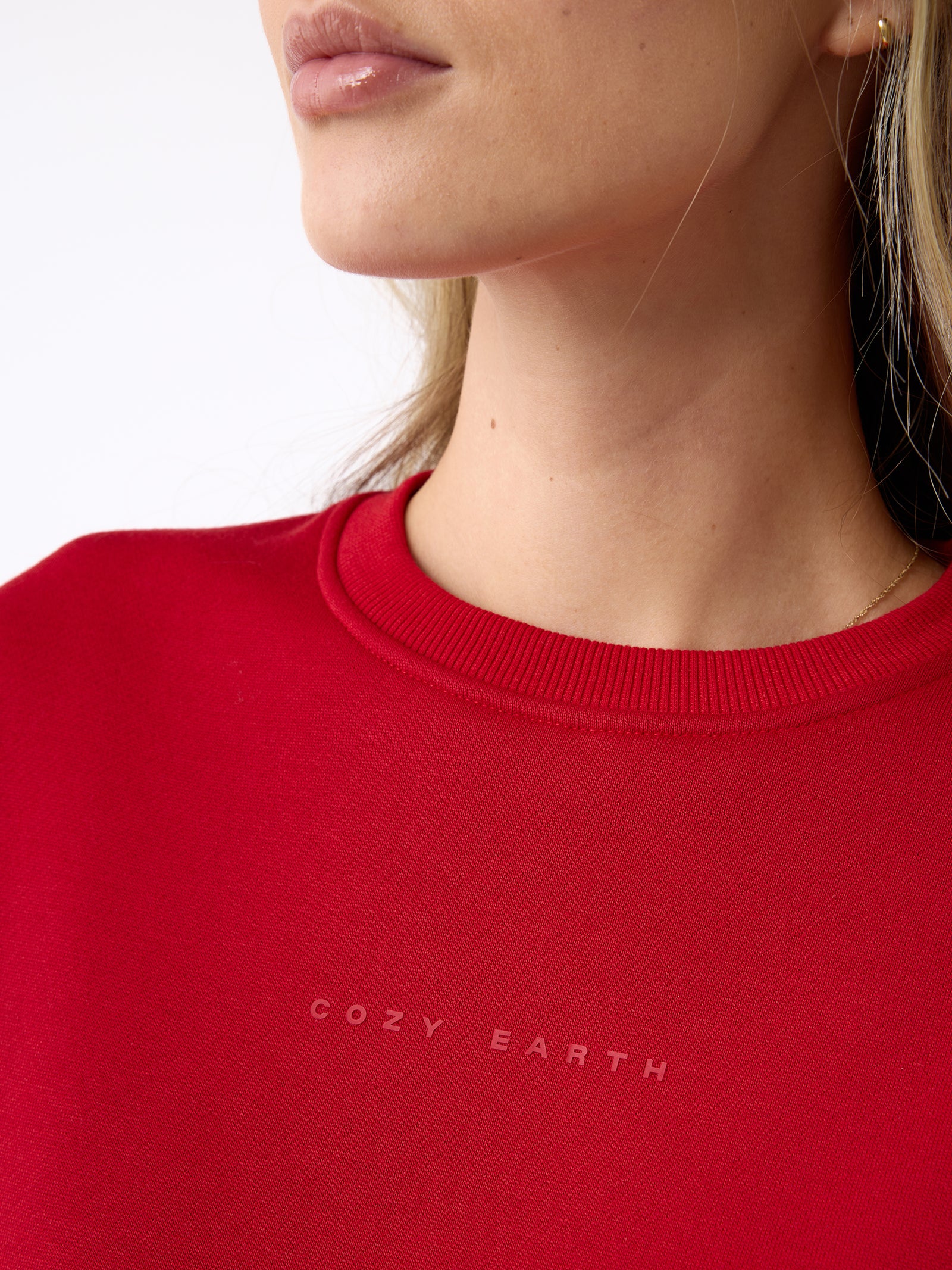 Close-up of a person wearing a red Women's CityScape Crewneck by Cozy Earth. The focus is on the neck and shoulders, showing minimal facial features against a plain white background. 