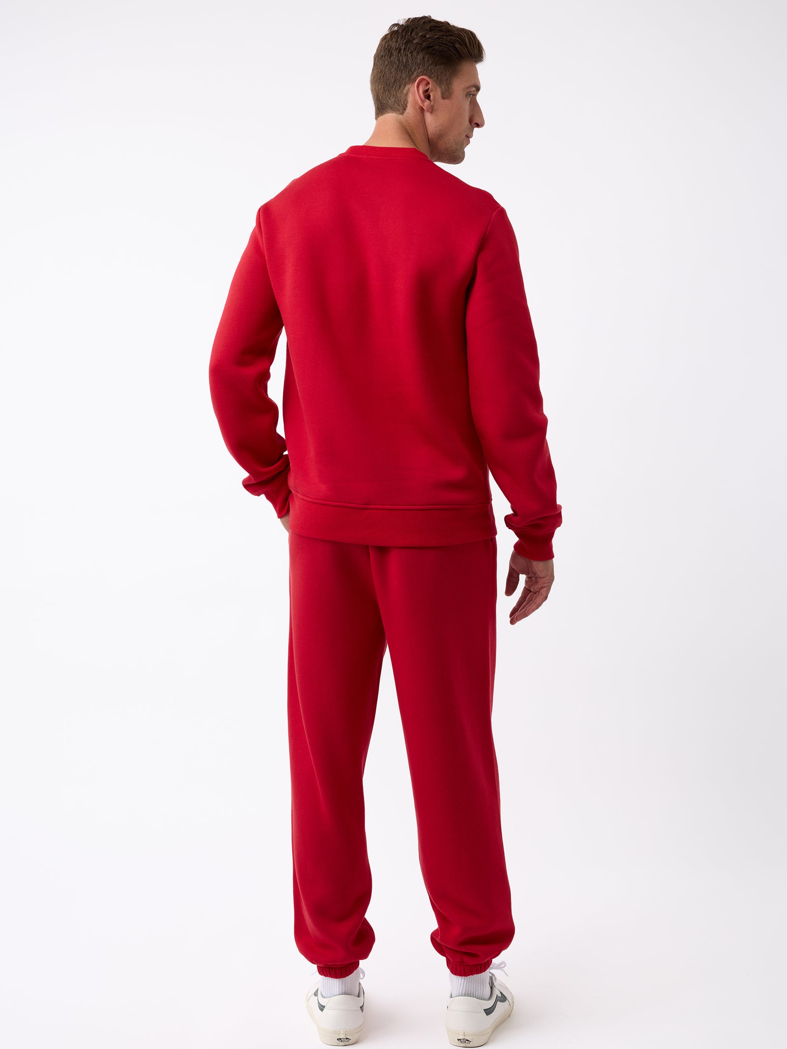 A person stands facing away, donning a matching red Men's CityScape Crewneck from Cozy Earth paired with white sneakers. The plain white background accentuates the vibrant color of the outfit. 