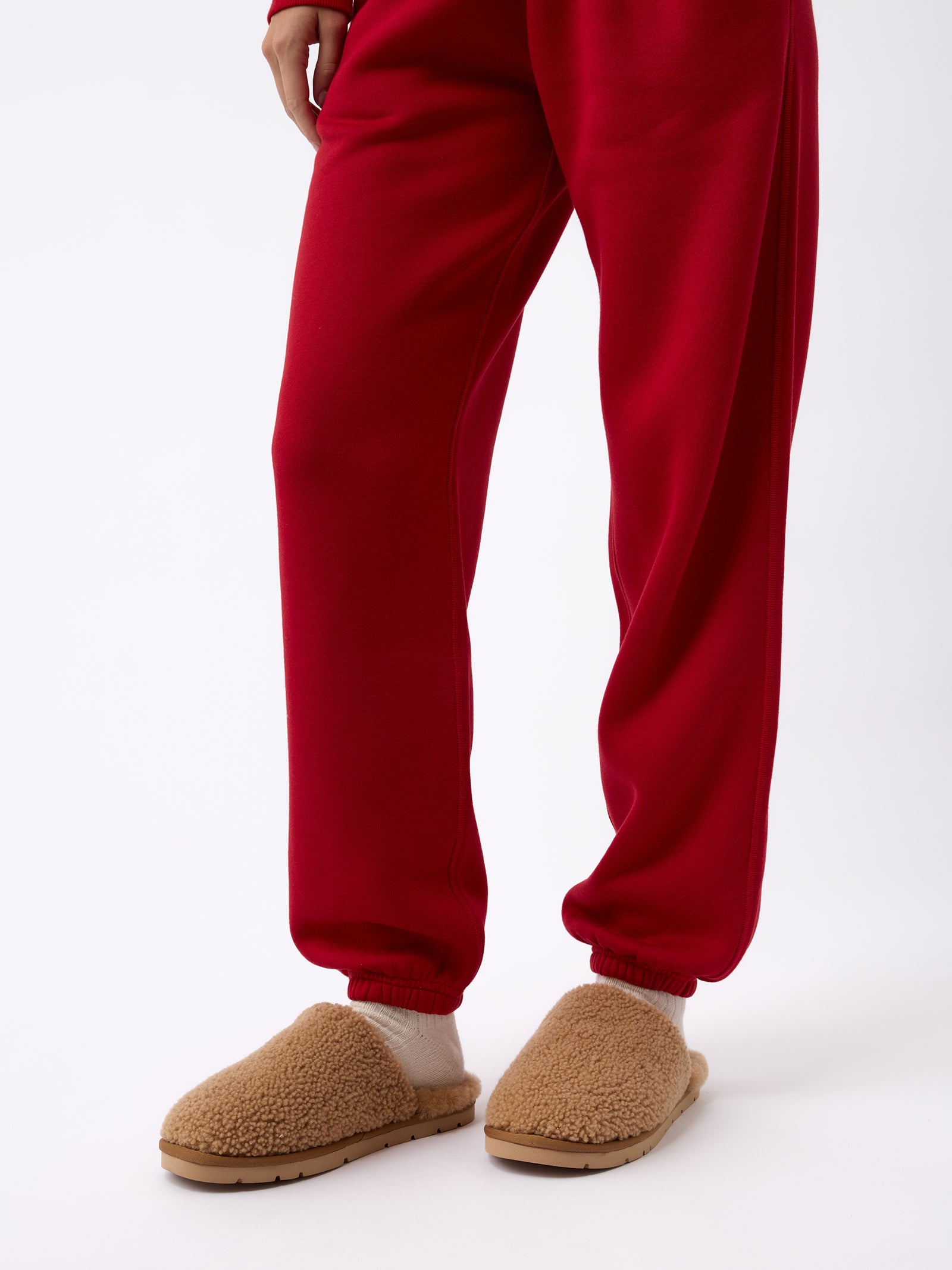 A person wearing plush tan slippers and Women's CityScape Sweatpant by Cozy Earth stands against a plain white background. The slippers appear soft and cozy, enhancing the casual, comfortable look. 