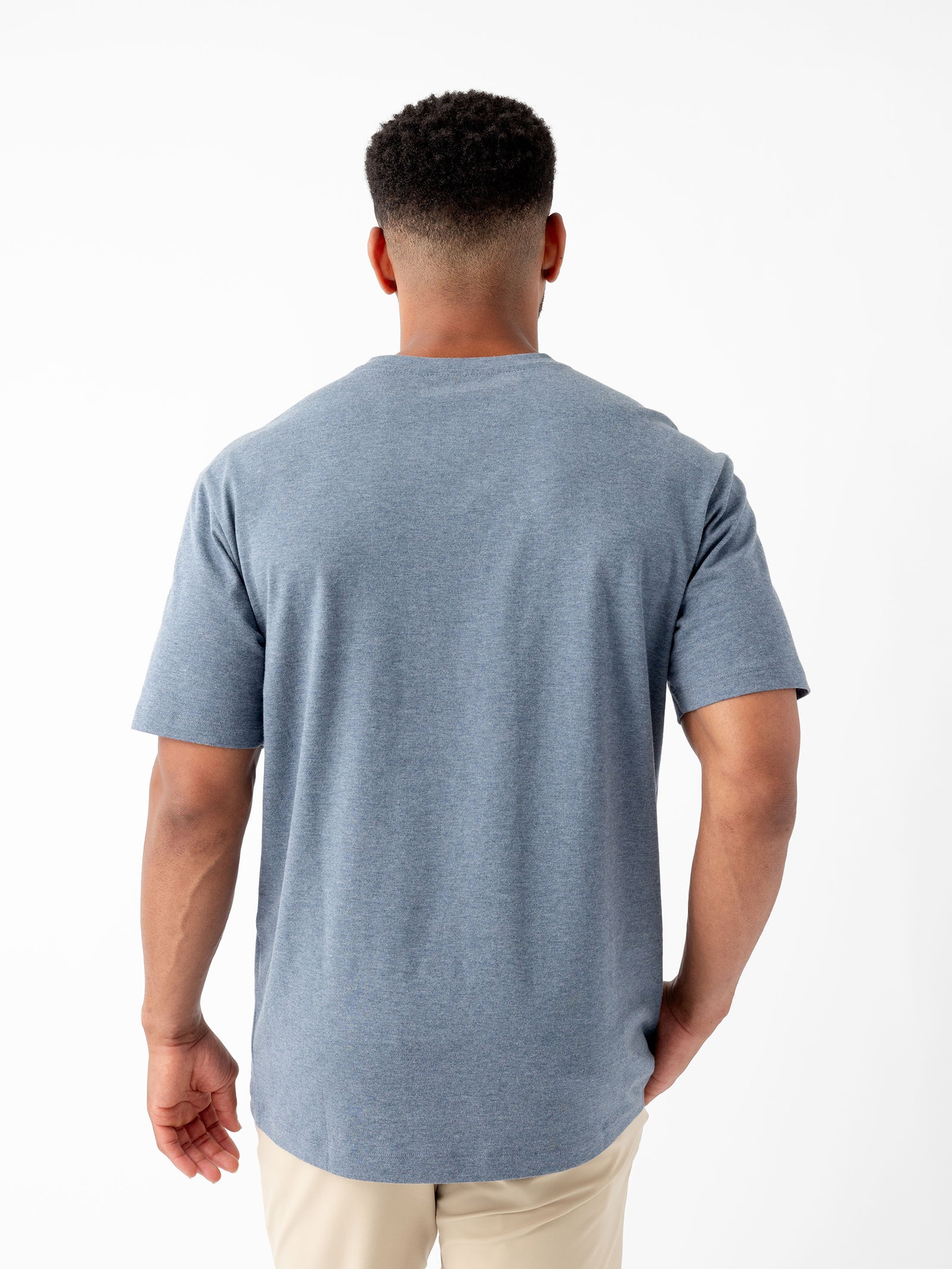 A man with short hair is seen from the back wearing a light blue short-sleeved Men's All Day Tee by Cozy Earth and beige pants. The background is plain white. 