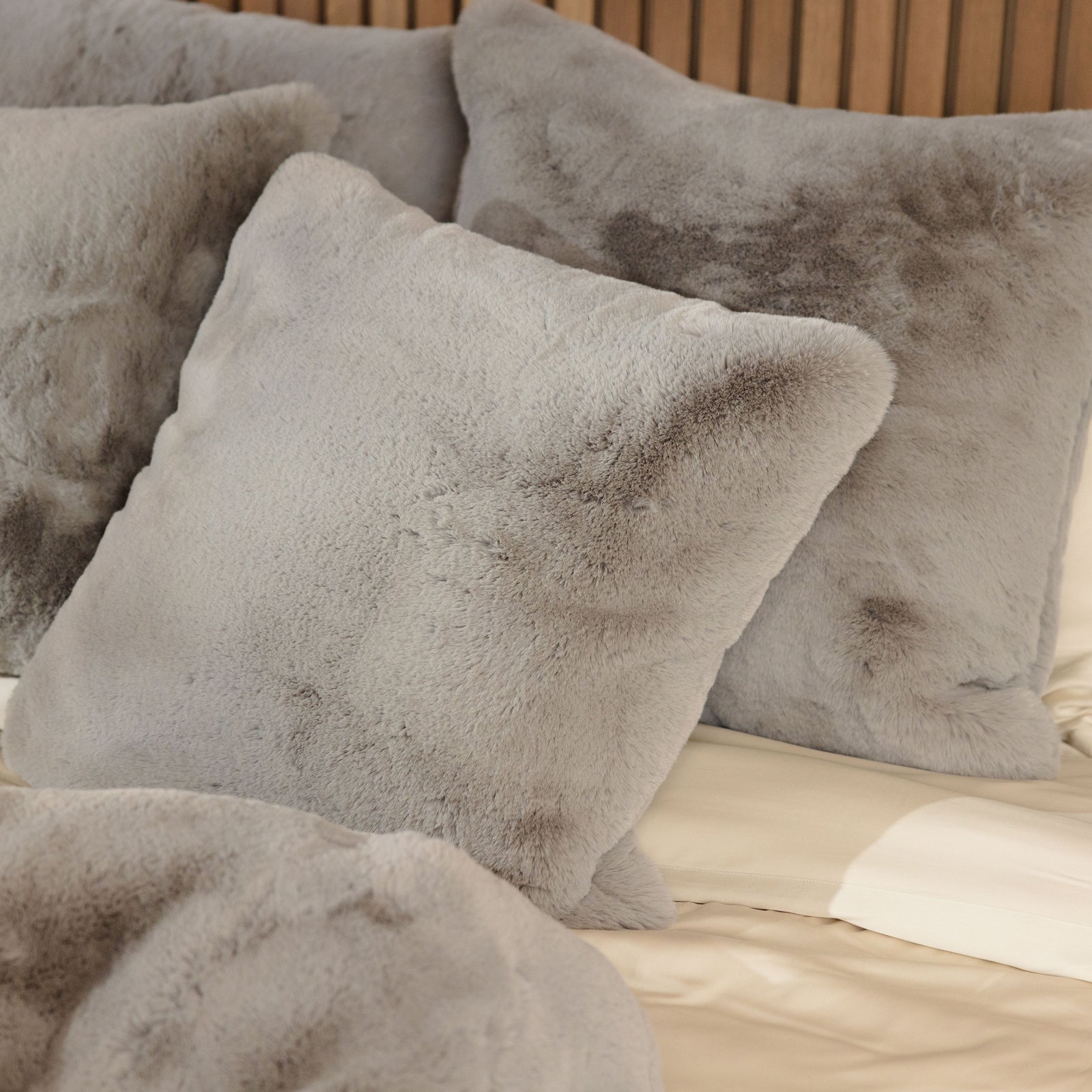 Cuddle Pillows by Cozy Earth, fluffy and light gray in color, are tastefully arranged on a beige bedspread against a wooden headboard. The soft texture of these pillows enhances the coziness of the bedroom setting. 