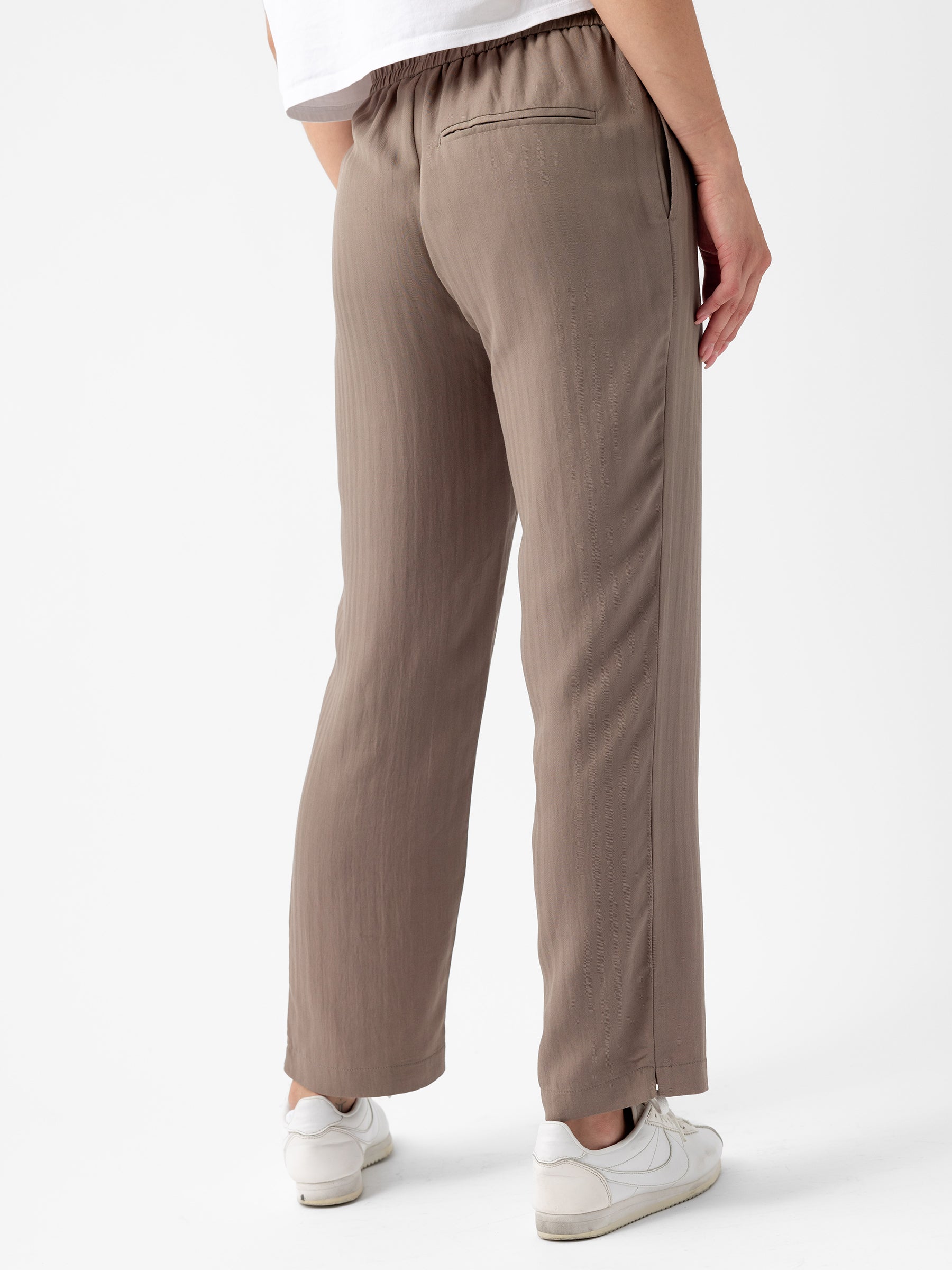 A person is shown from the back, wearing light brown Women's Sunset Cropped Pant from Cozy Earth and a white shirt. The pants have a relaxed fit and an elastic waistband. The person is also wearing white sneakers. The background is plain white. |Color:Ebony