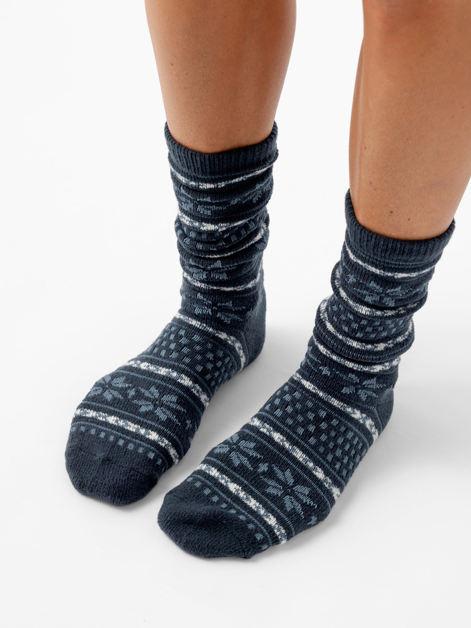 A person stands with a white background wearing Snowflake Plush Lounge Socks in Eclipse 