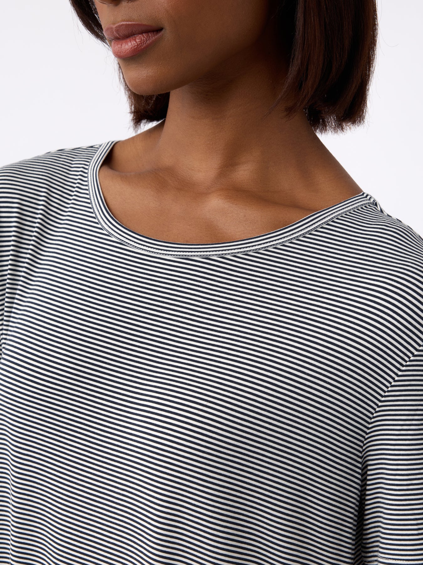 A close-up shows a person in the Women's Bamboo Stretch-Knit Sleep Dress by Cozy Earth. The black and white striped dress features a round neckline. A plain, light-colored background highlights the textured fabric and design. 