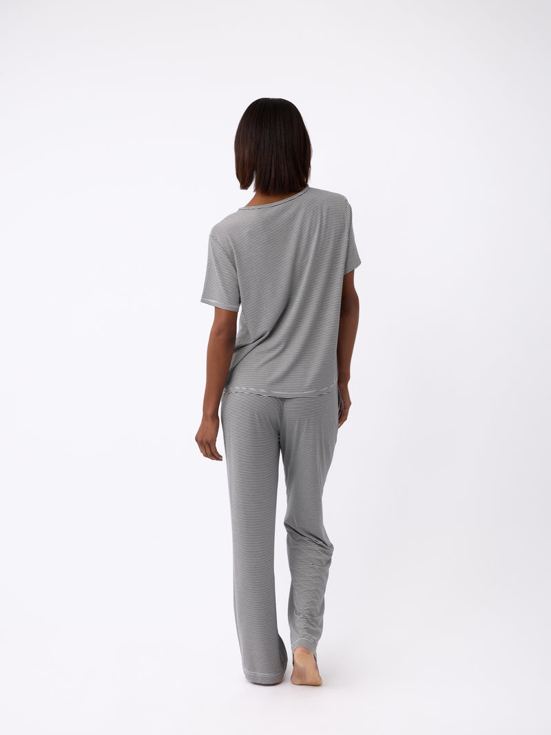 A person with shoulder-length hair stands barefoot, facing away, wearing a loose-fitting gray t-shirt along with Cozy Earth's Women's Bamboo Stretch-Knit Pant. The background is plain white.