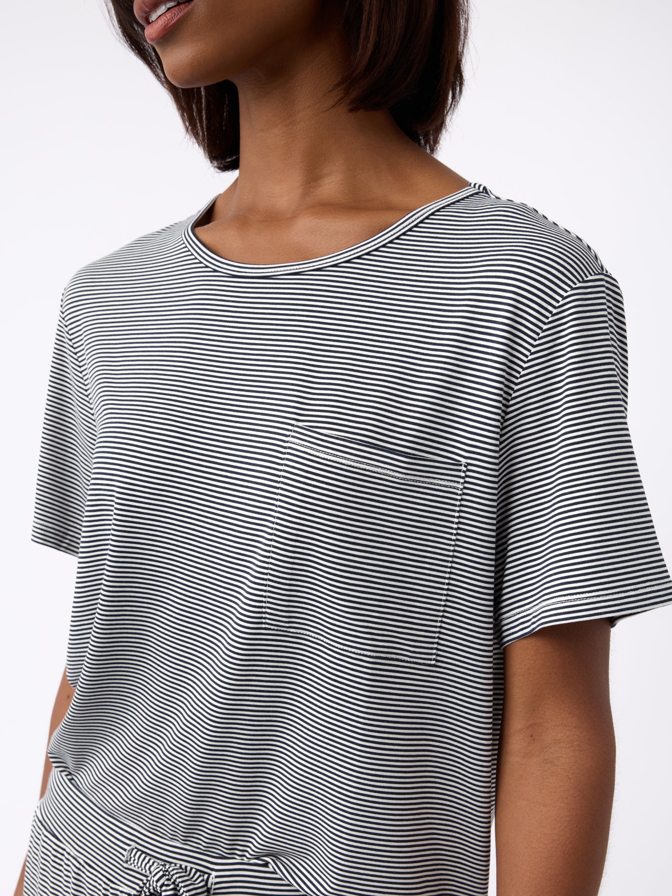 A person wearing Cozy Earth's Women's Bamboo Stretch-Knit Lounge Tee in black and white stripes with a pocket, featuring short sleeves and a round neckline against a plain white background. 