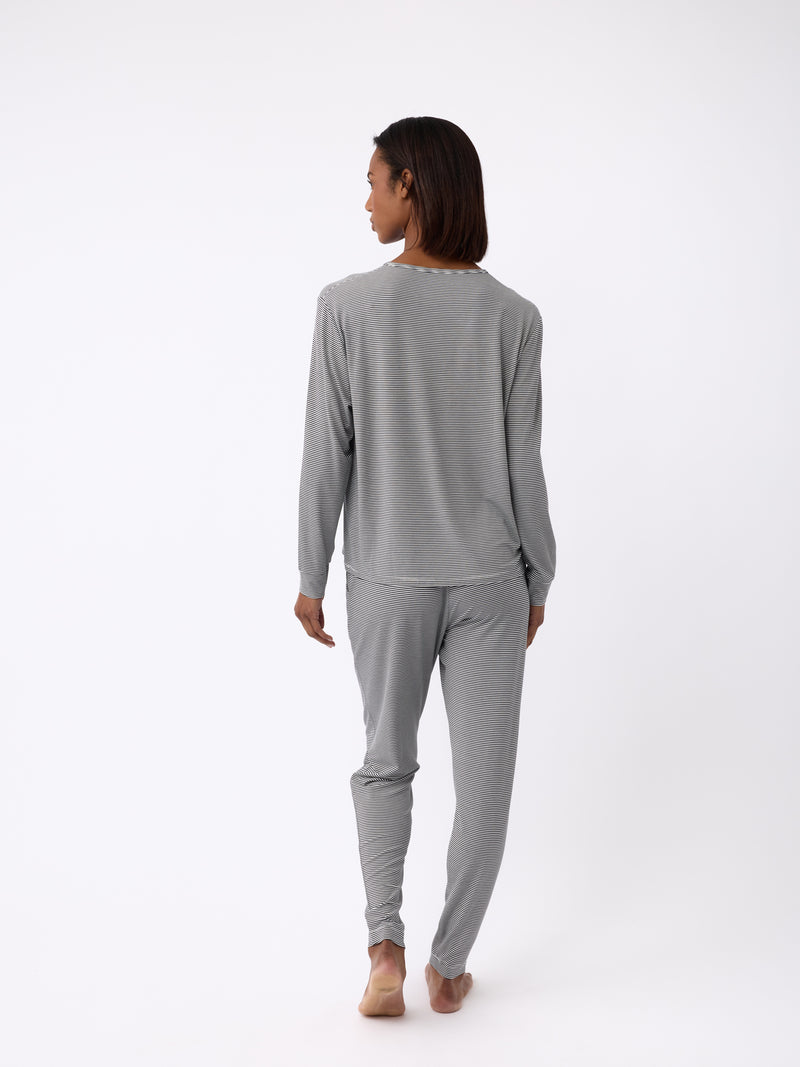 A person stands barefoot, facing away, wearing Cozy Earth's Women's Bamboo Stretch-Knit Tapered Pant in gray loungewear on a white background. The outfit includes a long-sleeve top and pants.