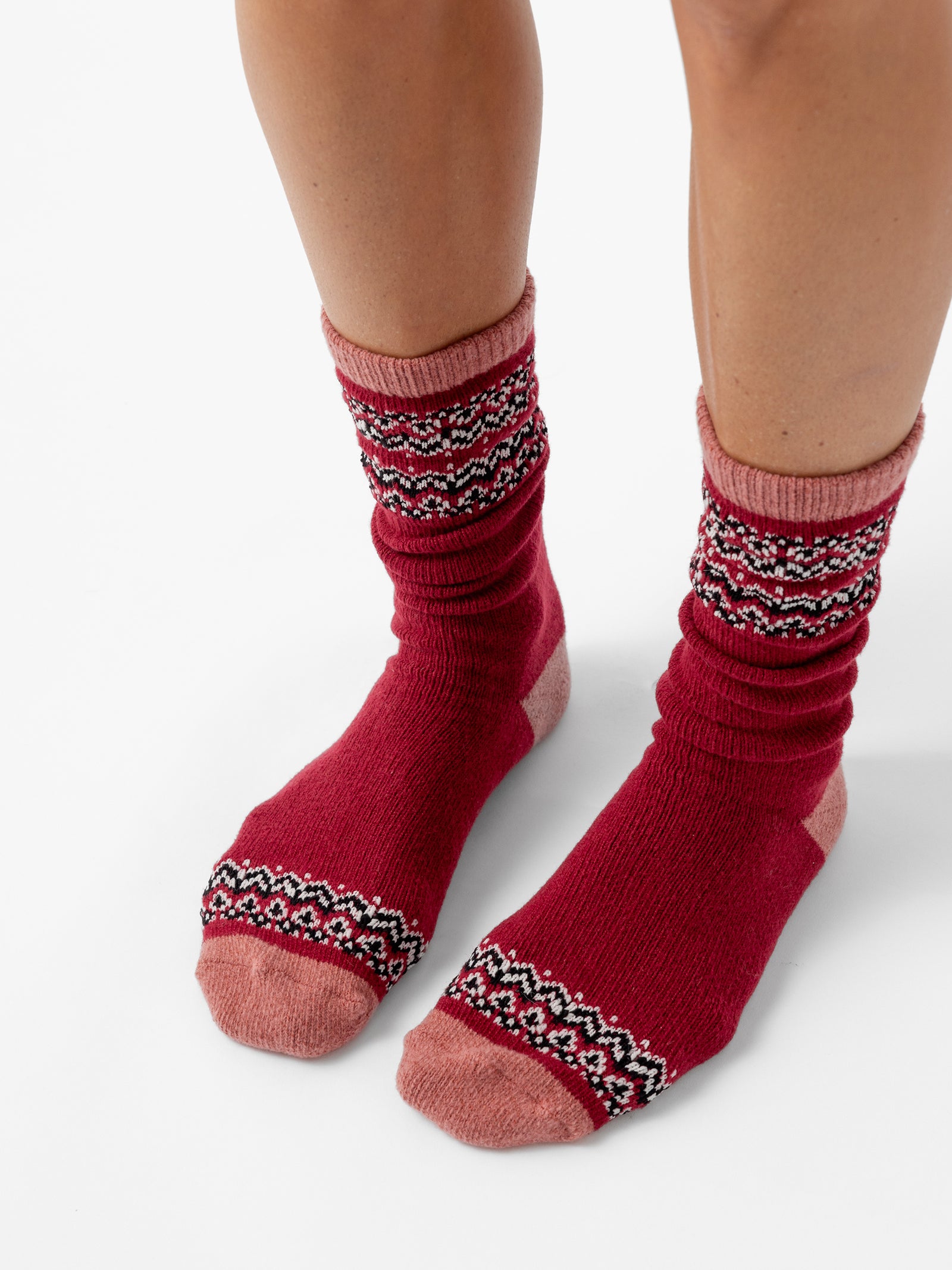 A person stands facing forward in front of a white background wearing Fair Isle Plush Lounge Socks in Garnet. 