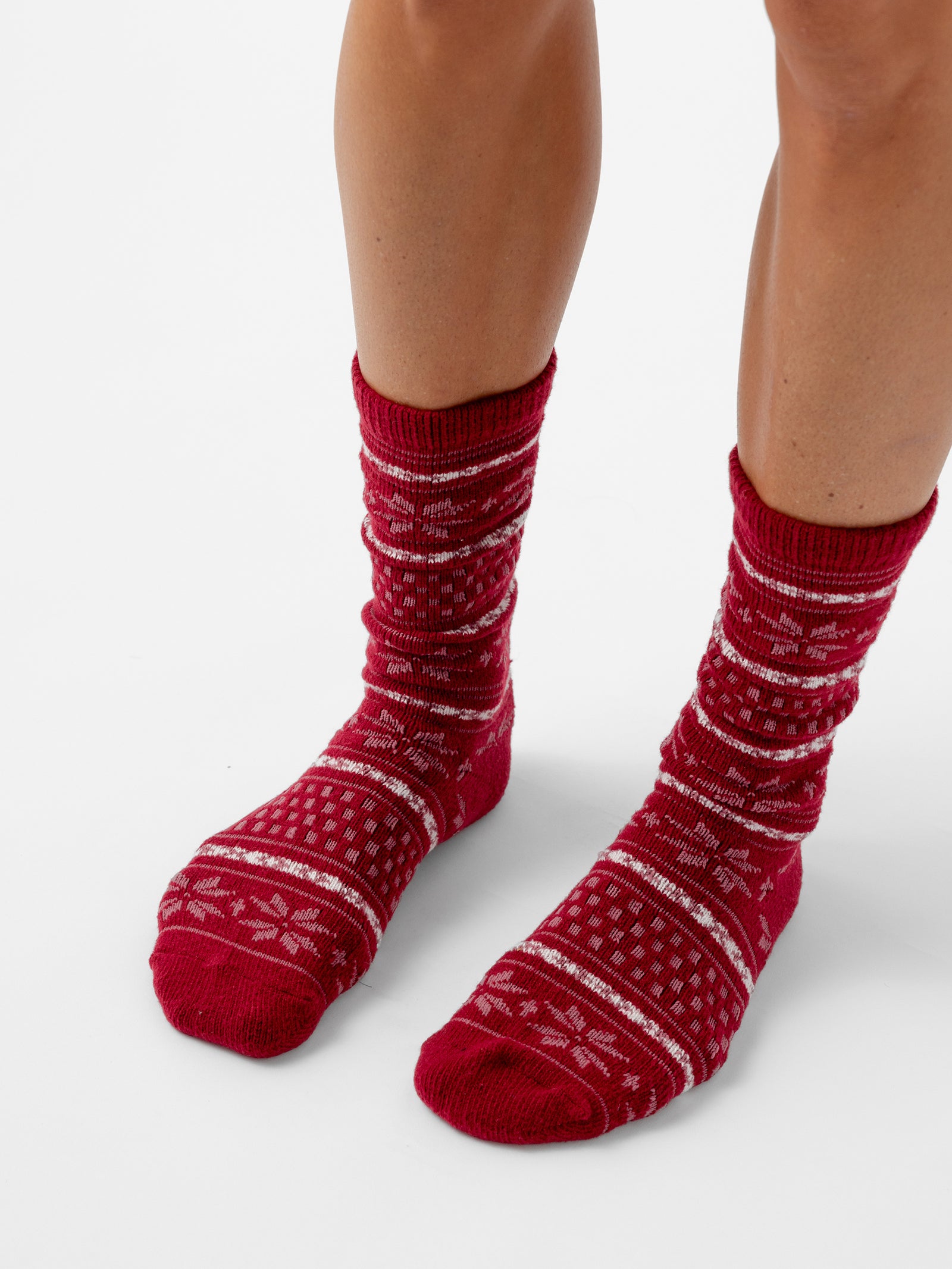 A person stands with a white background wearing Snowflake Plush Lounge Sock in Garnet 