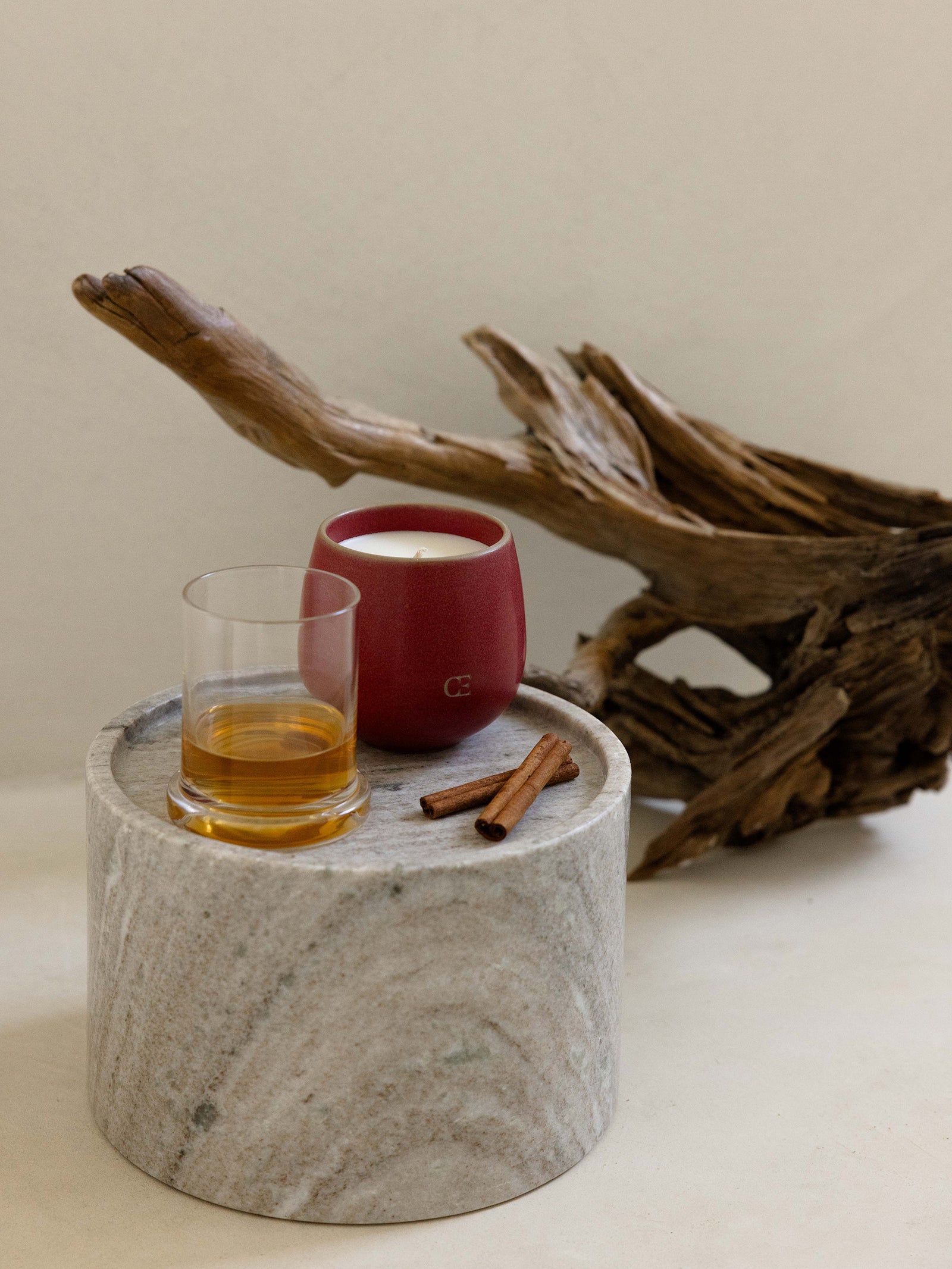 Cozy Earth Gather Candle sits with a tumbler and cinnamon sticks on a pedestal.