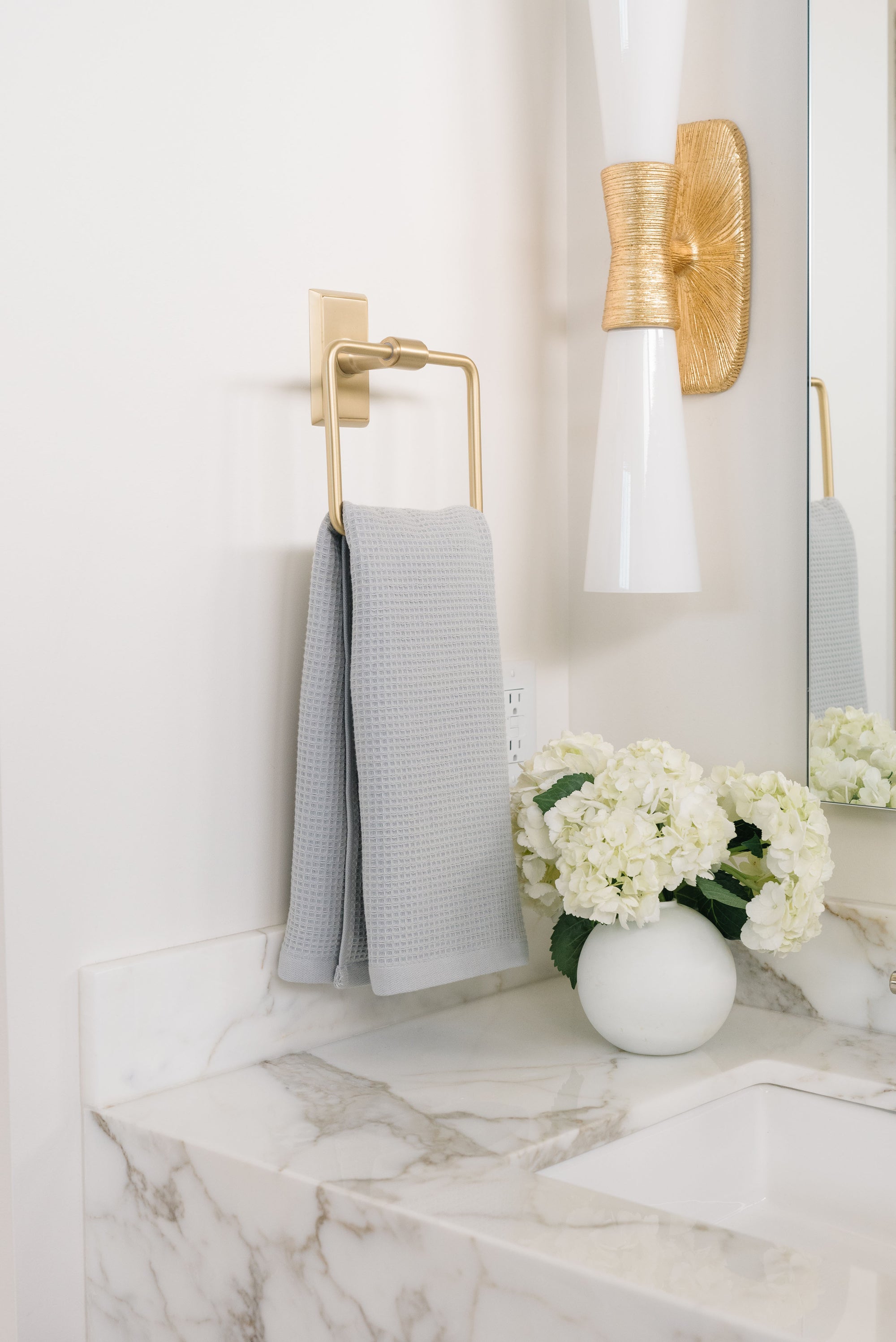 Harbor Mist Waffle Hand Towel hanging from a gold towel ring. The photo was taken at a white marble bathroom sink. 