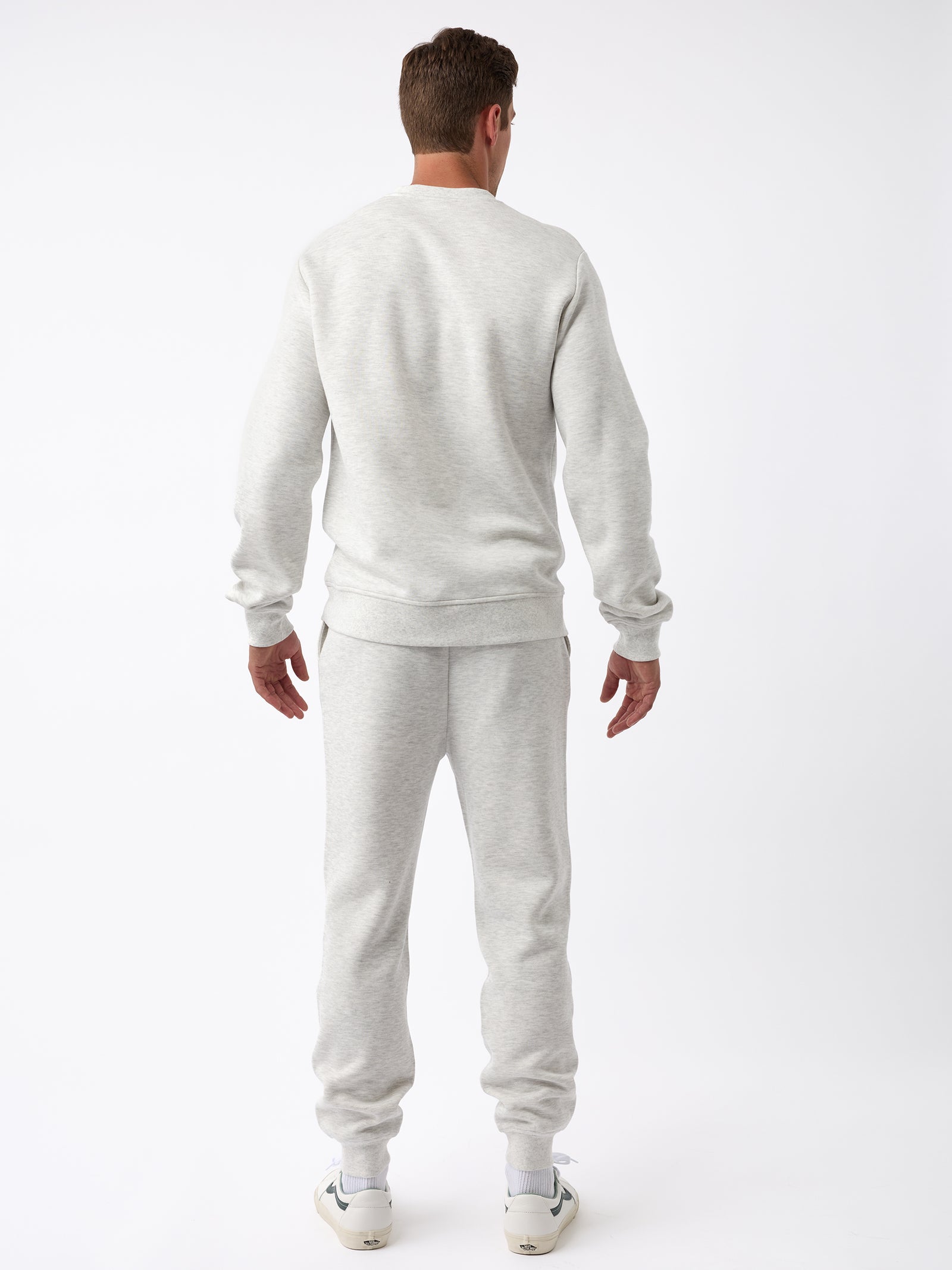 A person is wearing the Men's CityScape Jogger from Cozy Earth in a light gray color, paired with white sneakers, and is facing away from the camera against a plain white background. 