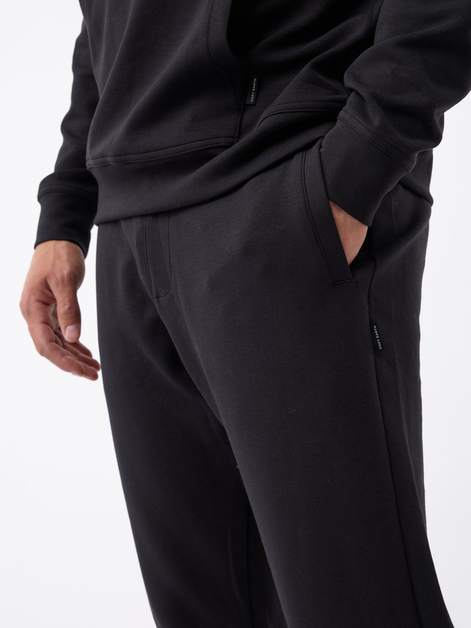 A person wearing a black sweatshirt and Cozy Earth's Men's StretchTech Jogger in black stands with one hand in their pocket. The focus is on the lower half of the torso and upper legs, highlighting the casual and comfortable style of the outfit. The background is plain white. 