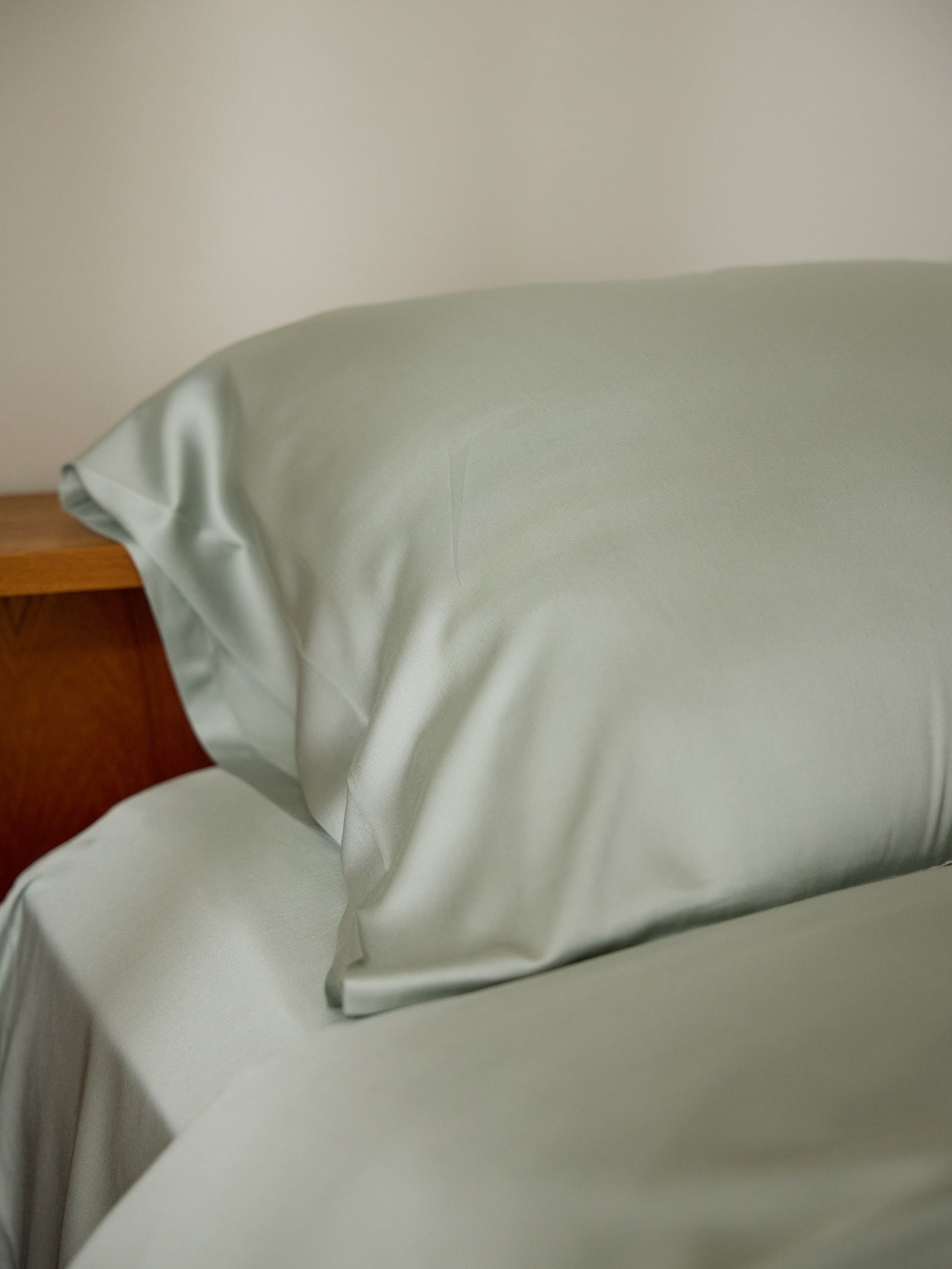 A neatly made bed featuring Cozy Earth's light green Bamboo Pillowcases and sheets, set against a wooden headboard, conveying comfort and relaxation. 