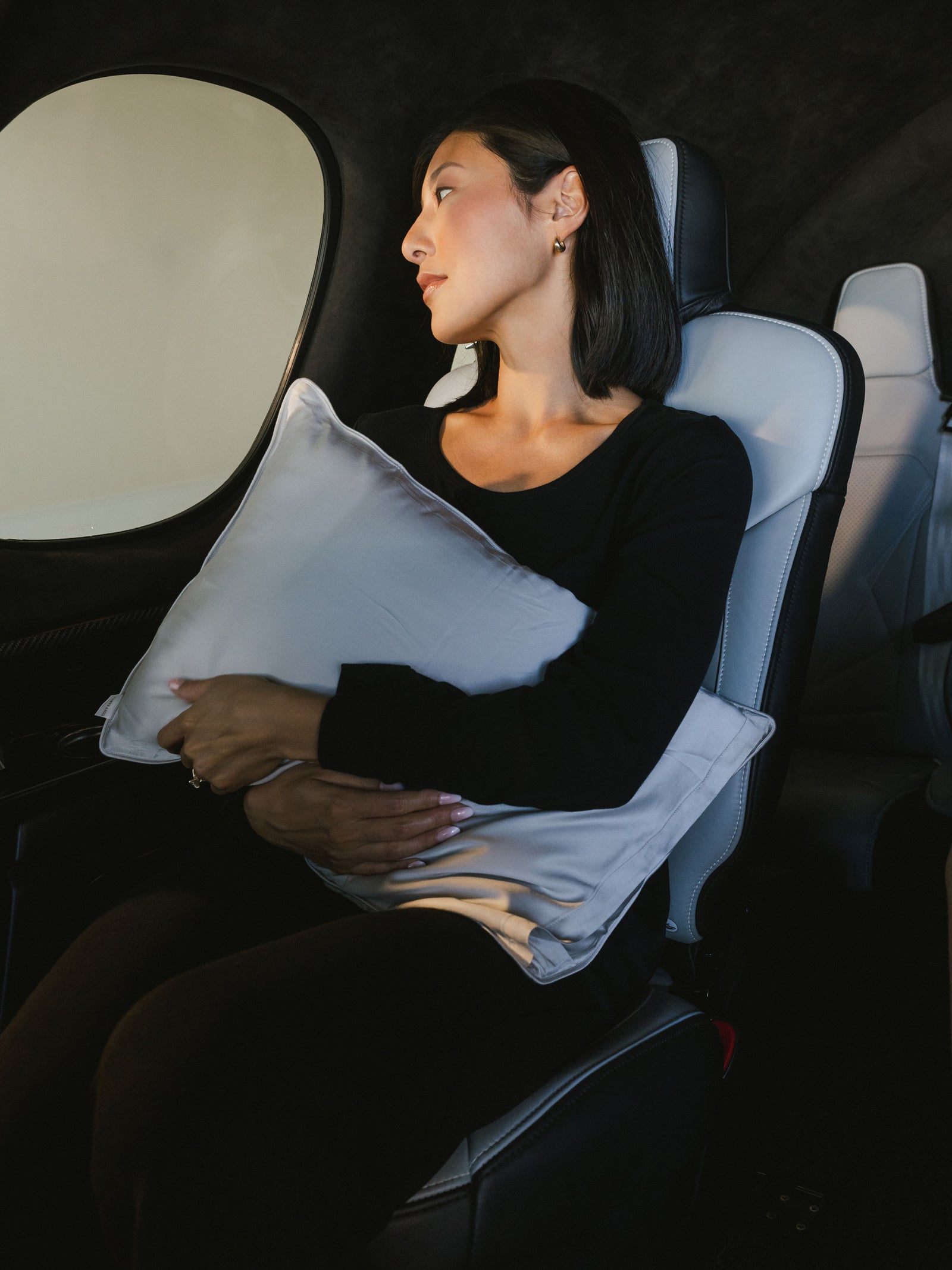 Woman in car holding travel pillow with light grey case in her lap 