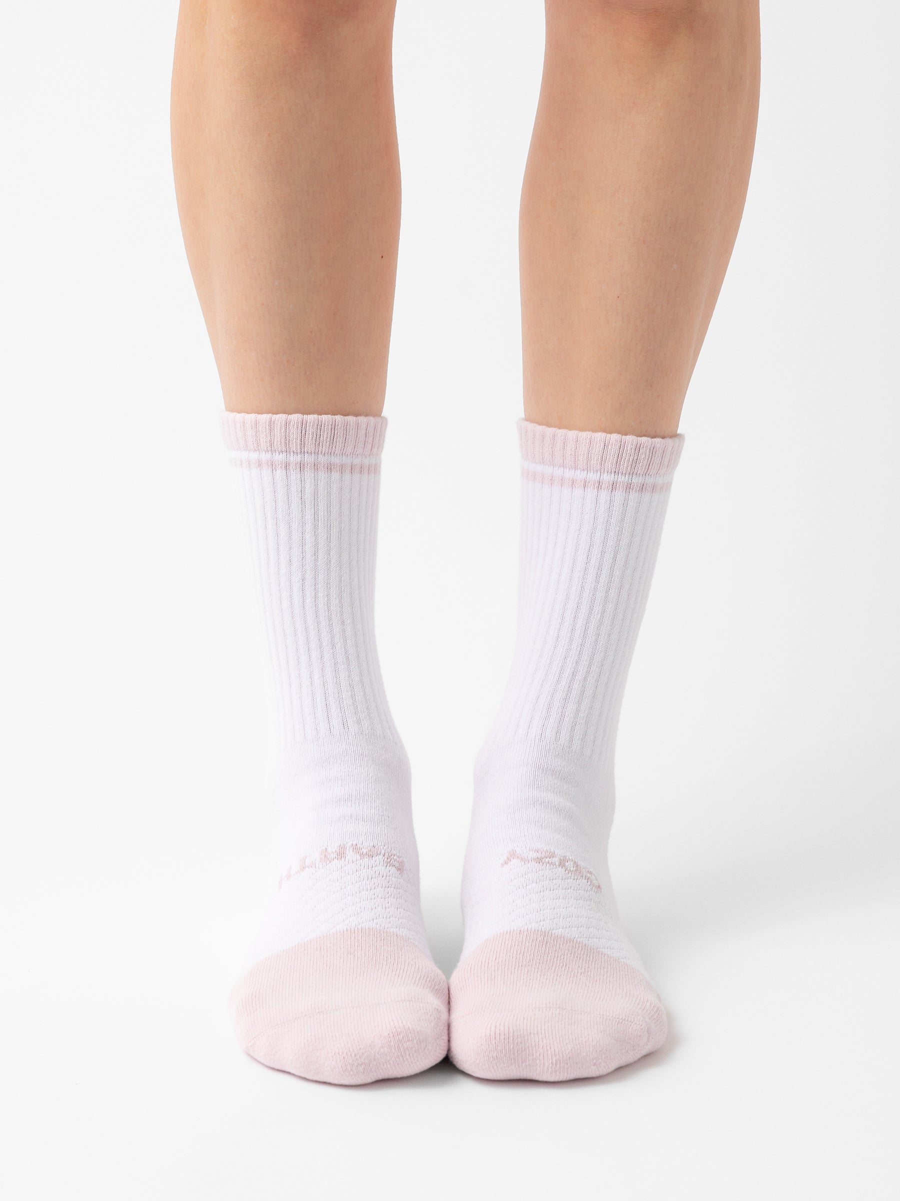 A person wearing Cozy Earth's Essential Calf Socks, in white with faint pink toes, is standing on a white surface. The socks feature ribbed cuffs and subtle pink stripes near the top. |Color:Lilac