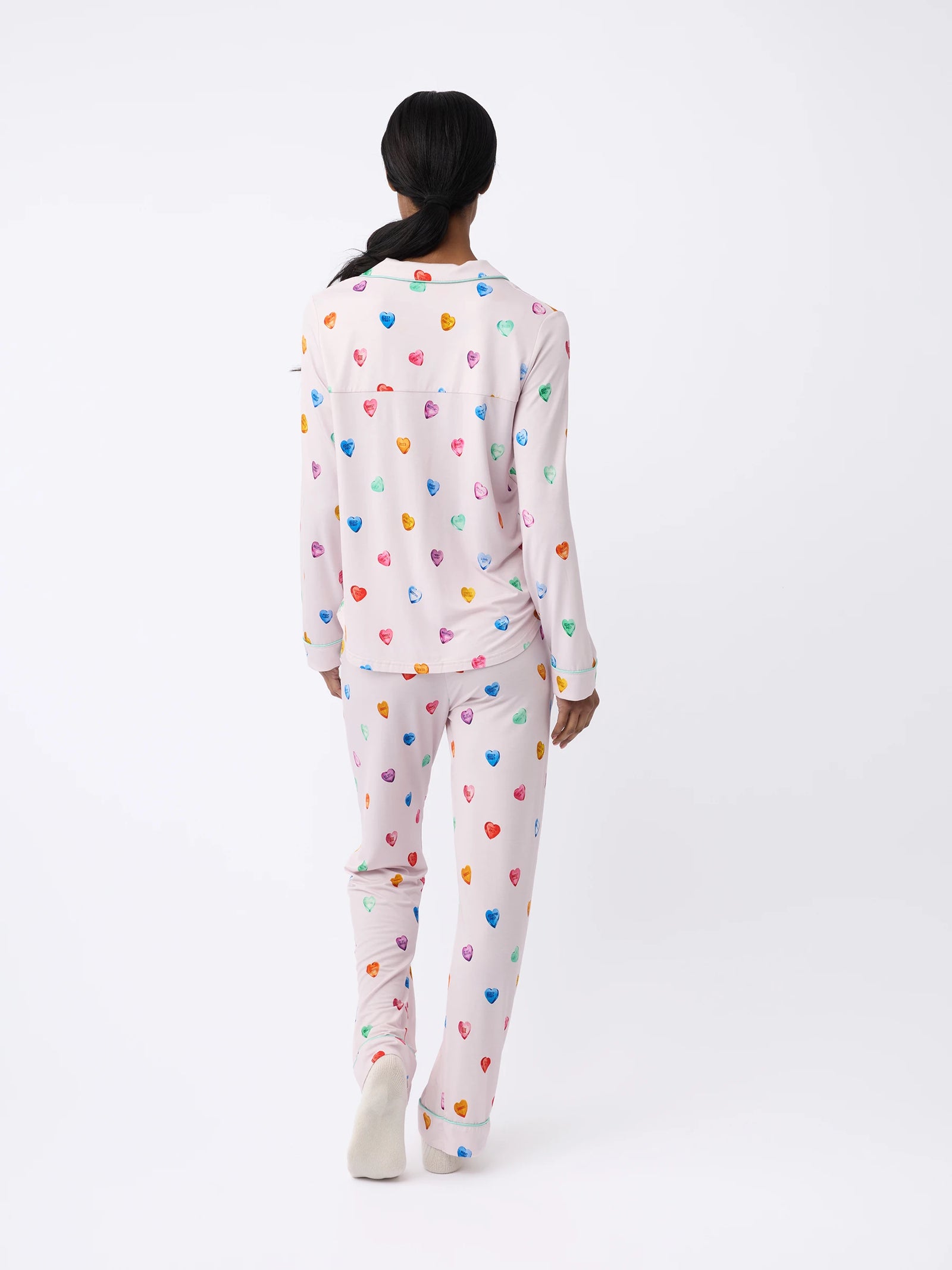 A person wearing Cozy Earth Women's Long Sleeve Bamboo Pajama Top in Stretch-Knit with a colorful heart pattern stands facing away against a plain white background. 