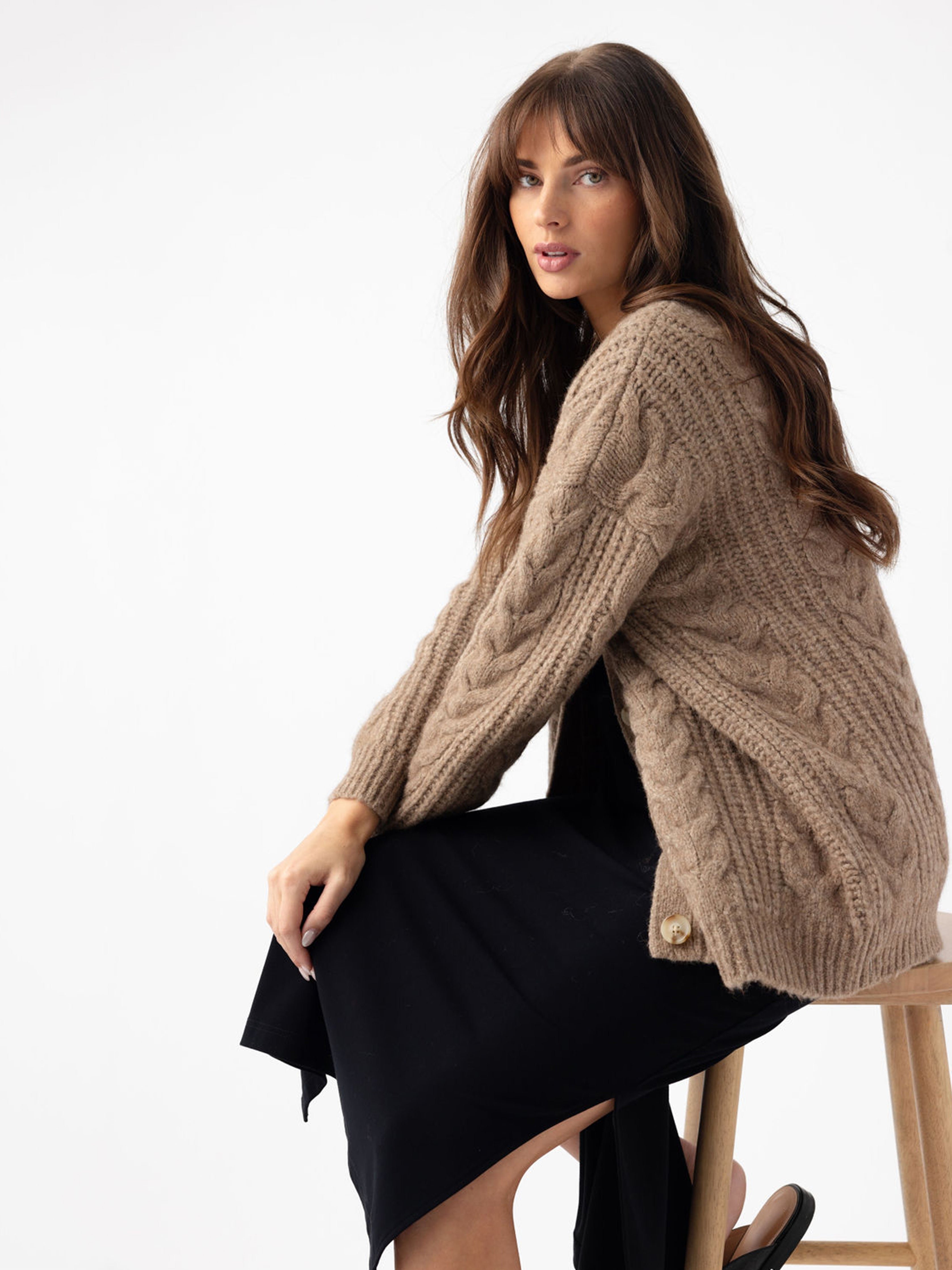 Woman sitting on wooden stool with black dress and mushroom cardigan 