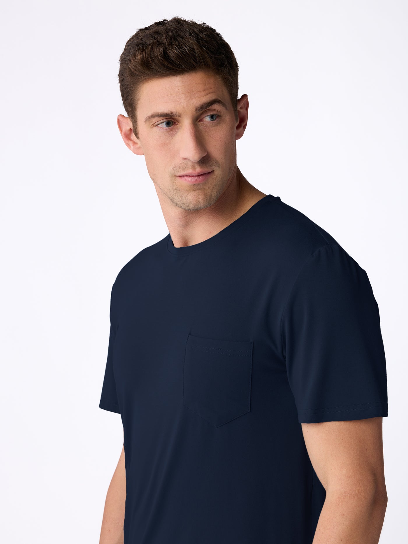 A man with short brown hair wears the Cozy Earth Men's Bamboo Stretch-Knit Short Sleeve Pajama Set in dark navy blue with a chest pocket, standing against a light background and looking to his left. 