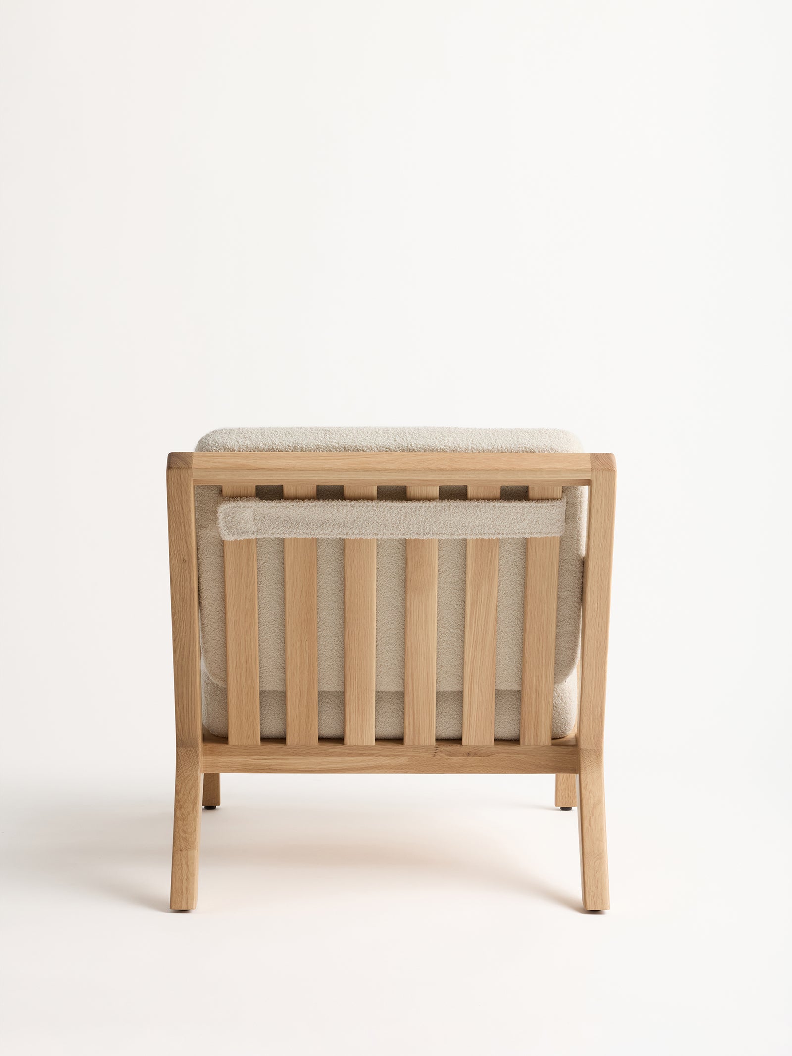 The Coronado Lounge Chair by Cozy Earth is displayed from the back, showcasing its simple, modern wooden design with vertical slats and a light beige cushion on the seat and backrest, all set against a neutral background. 