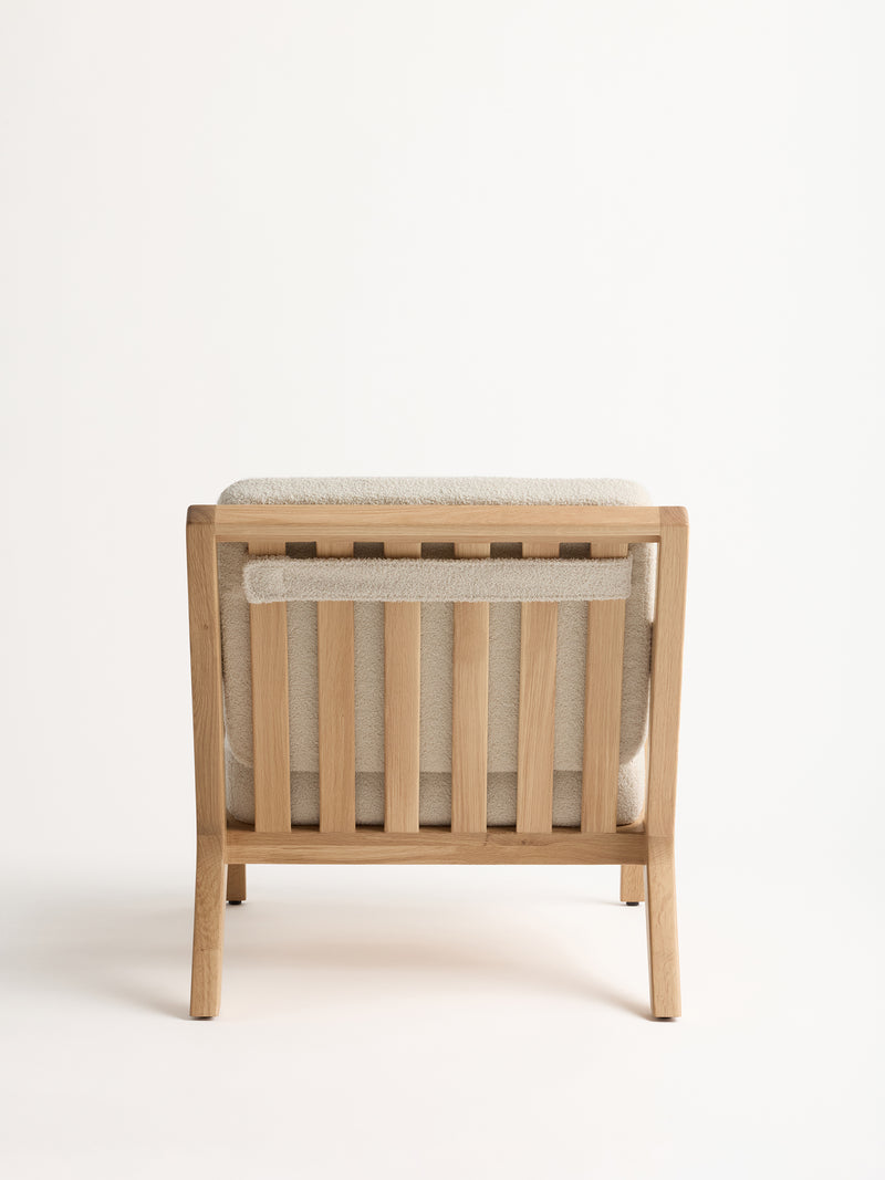 The Coronado Lounge Chair by Cozy Earth is displayed from the back, showcasing its simple, modern wooden design with vertical slats and a light beige cushion on the seat and backrest, all set against a neutral background.