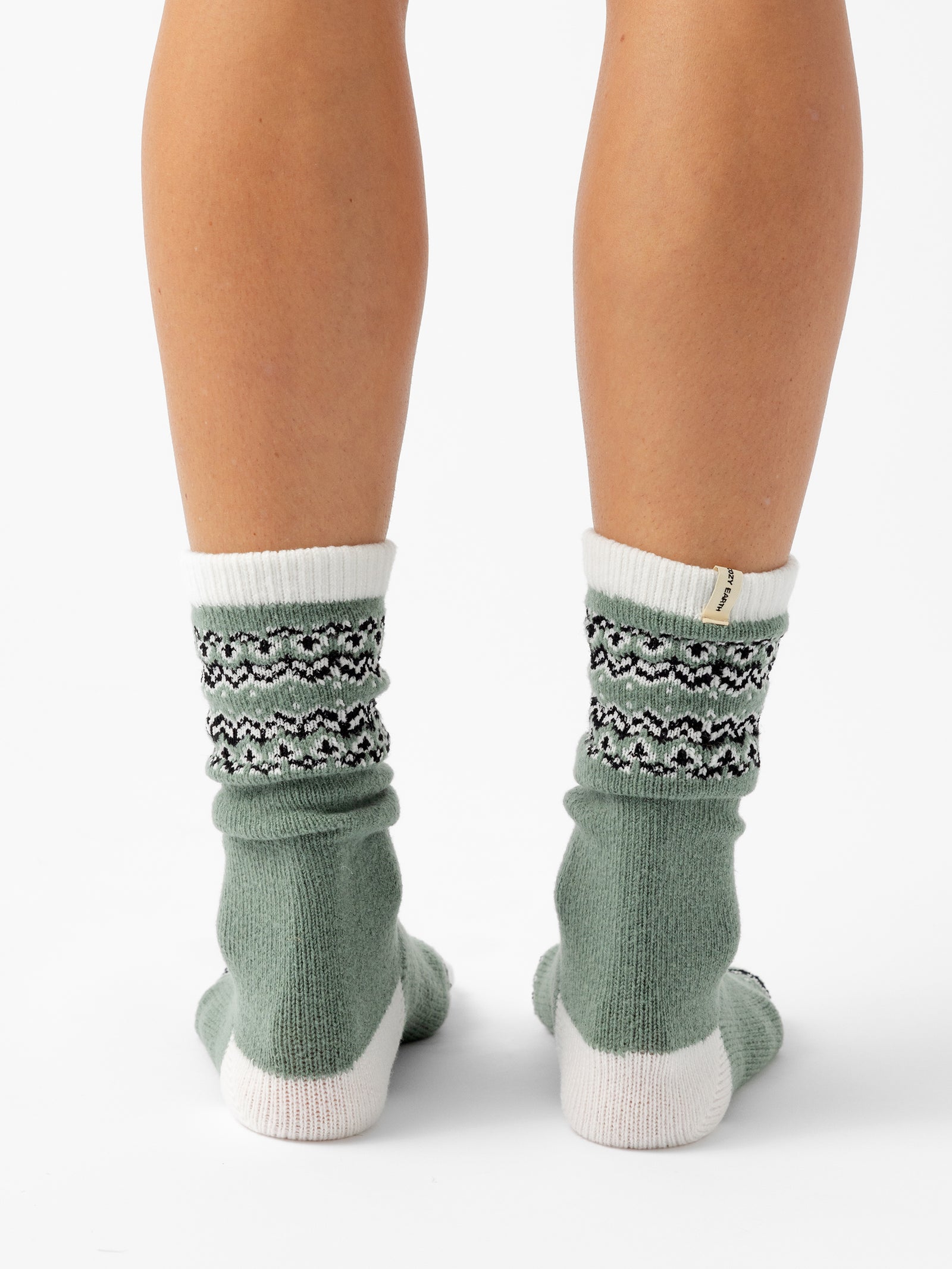 A person stands facing backwards in front of a white background wearing Fair Isle Plush Lounge Socks in Oakmoss. 