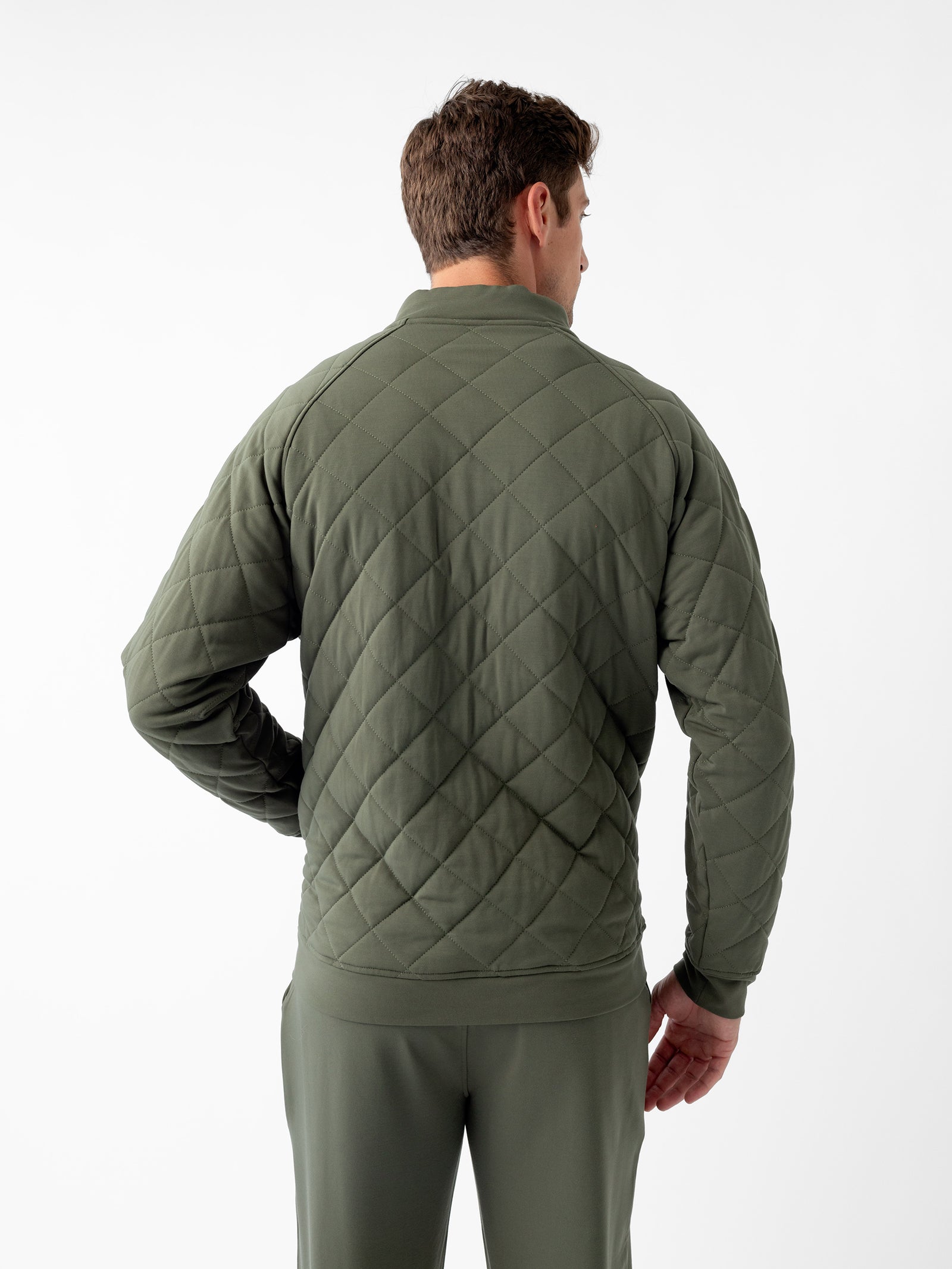 A man wearing a Cozy Earth Men's Ultra-Soft Bamboo Quilted Snap Pullover in olive green and matching pants is standing with his back facing the camera against a plain white background. The pullover features a diamond pattern and has a high collar. His short hair is styled neatly. 