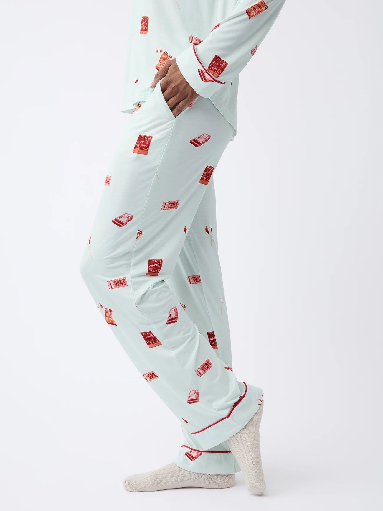 A person in Cozy Earth Women's Stretch-Knit Bamboo Pajama Pant, light blue with red and white match books, stands on a white backdrop. 