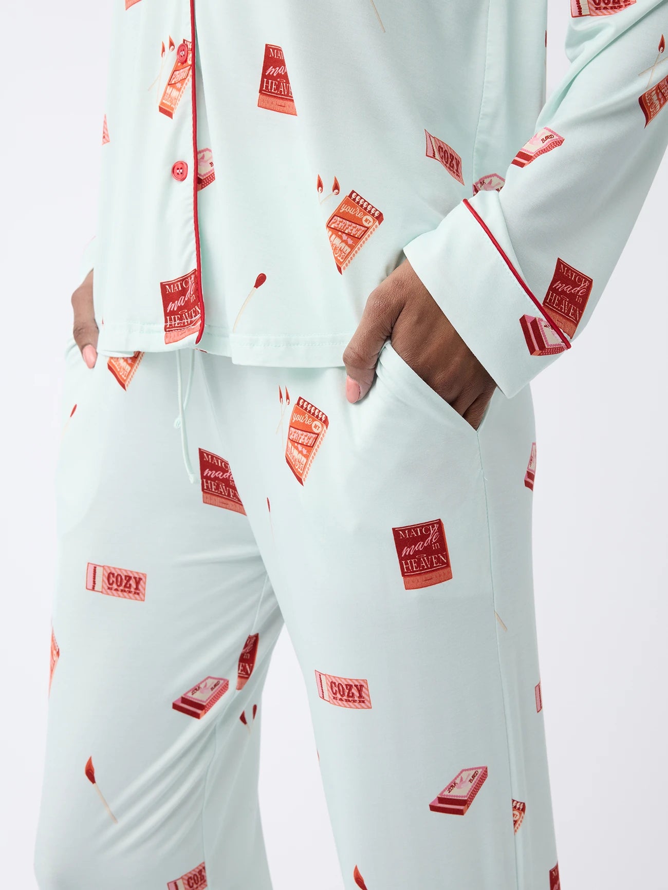 A woman is wearing a Cozy Earth Women's Stretch-Knit Long Sleeve Bamboo Pajama Set in light green with a matchbox pattern and red and white accents, one hand in their pocket, and red piping on the sleeves. 