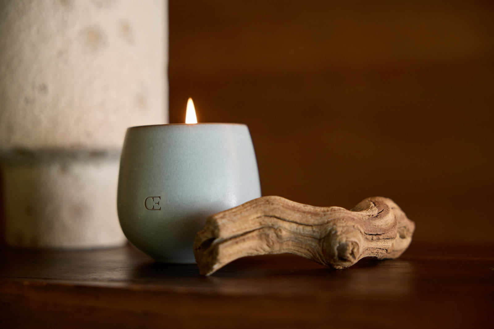 Cozy Earth Revive Candle lit on a shelf next to a piece of driftwood