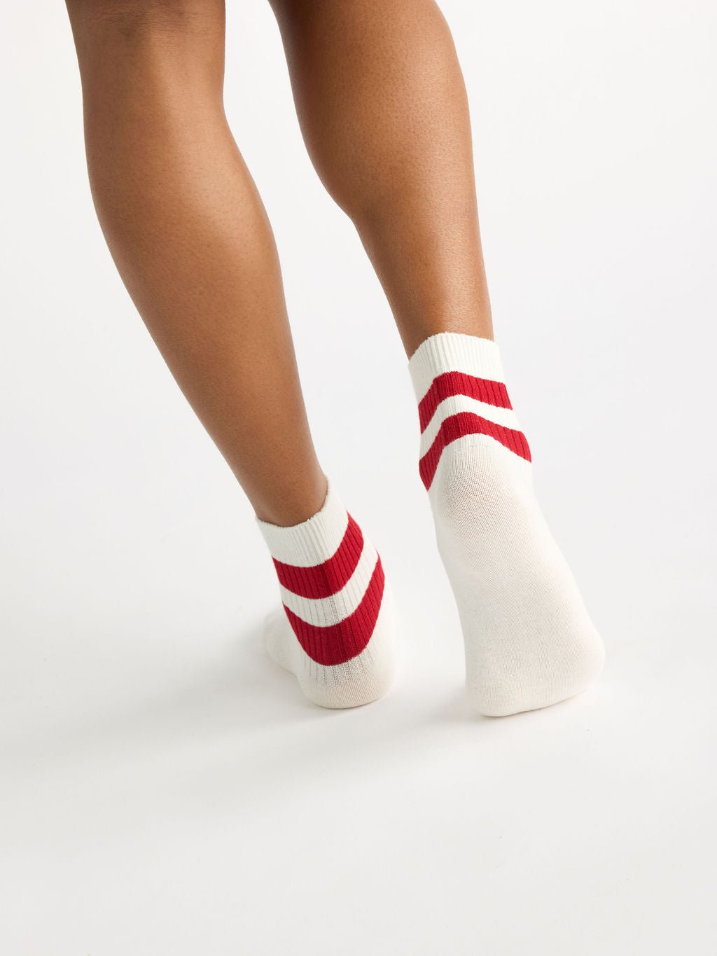 A person wearing Cozy Earth's Women's Sadie Sock featuring two red horizontal stripes on the back, stands with legs slightly apart against a plain white background. 