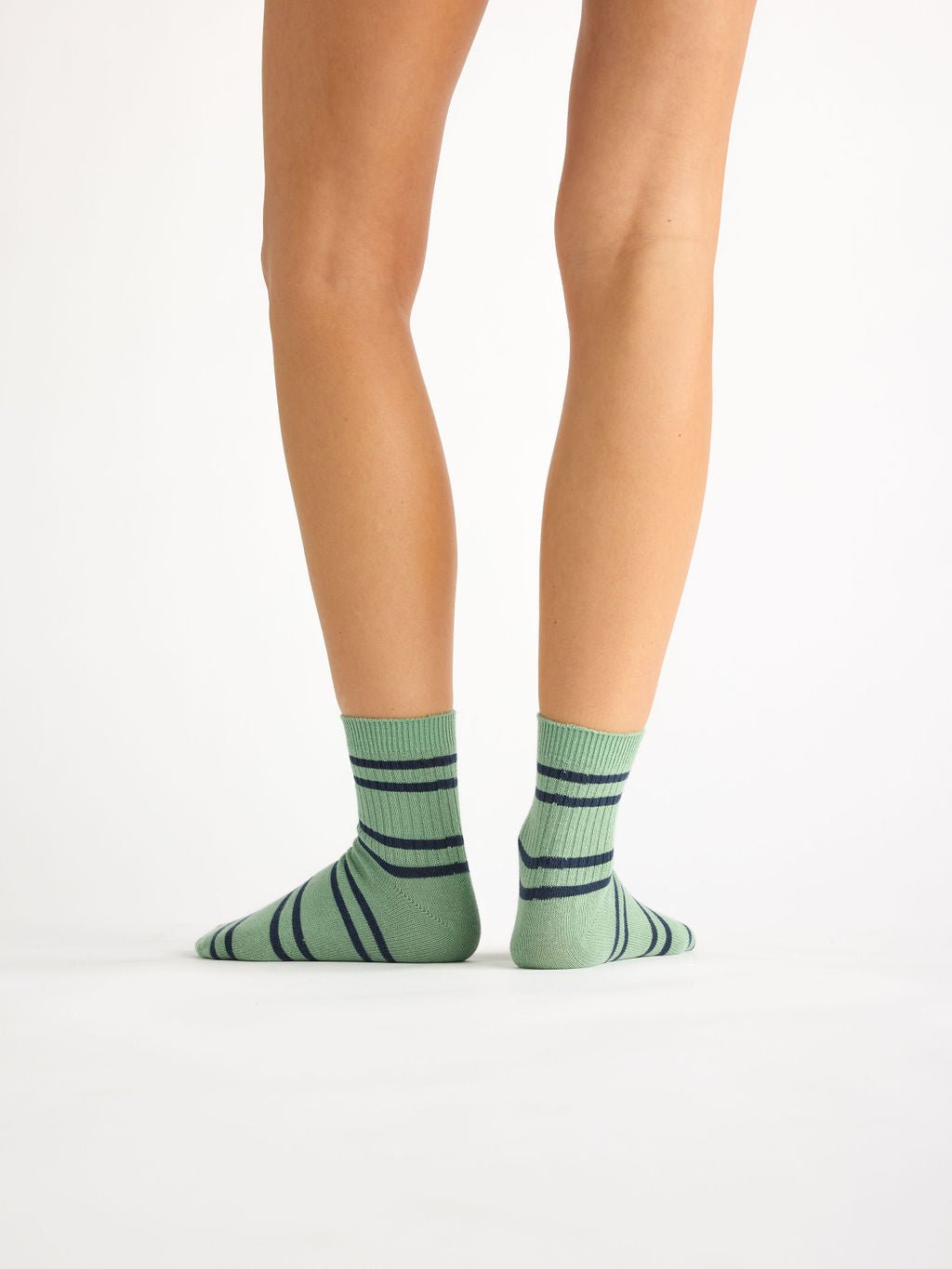 A person faces away from the camera, showcasing Cozy Earth's Women's Sadie Sock in green with dark blue horizontal stripes against a plain white background. 