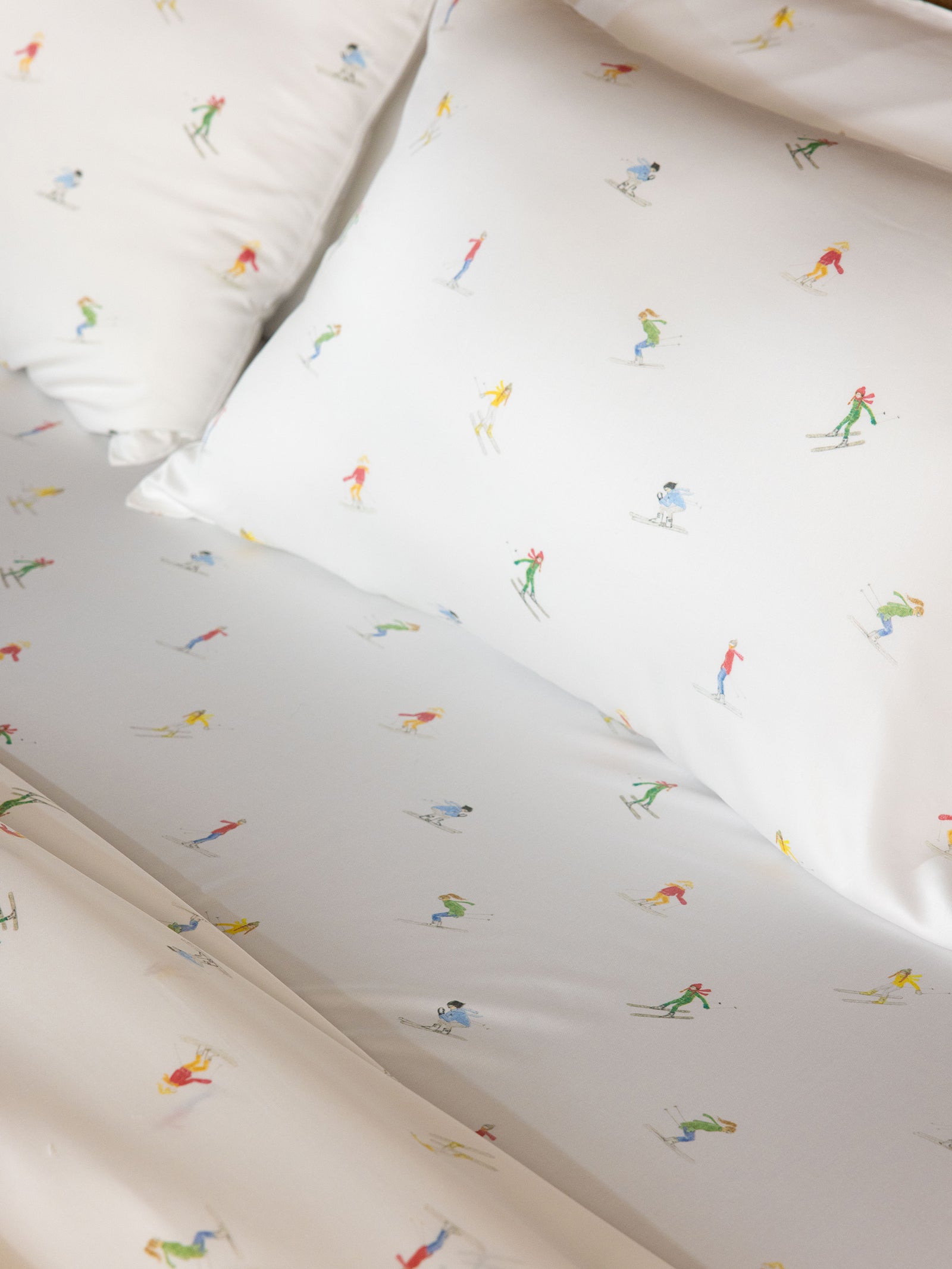 Cozy Earth's Bamboo Sheet Set in white features vibrant and playful illustrations of skiers in various poses scattered across the smooth fabric. 