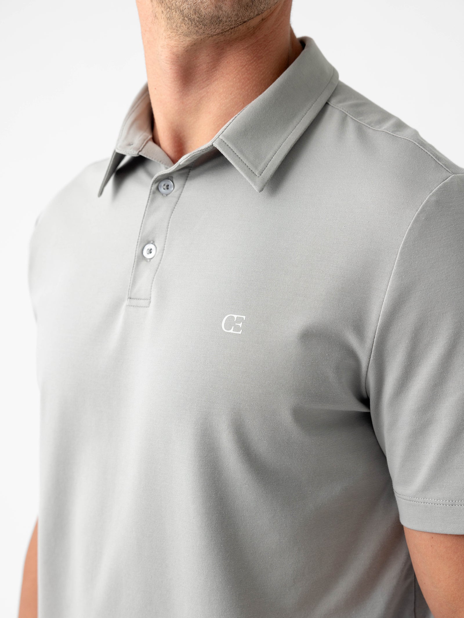 A man wearing the Cozy Earth Men's Everyday Polo, featuring a light gray color and adorned with a small, white logo on the chest. The shirt has a collar and two visible buttons, against a plain background. Only his upper torso is shown. 