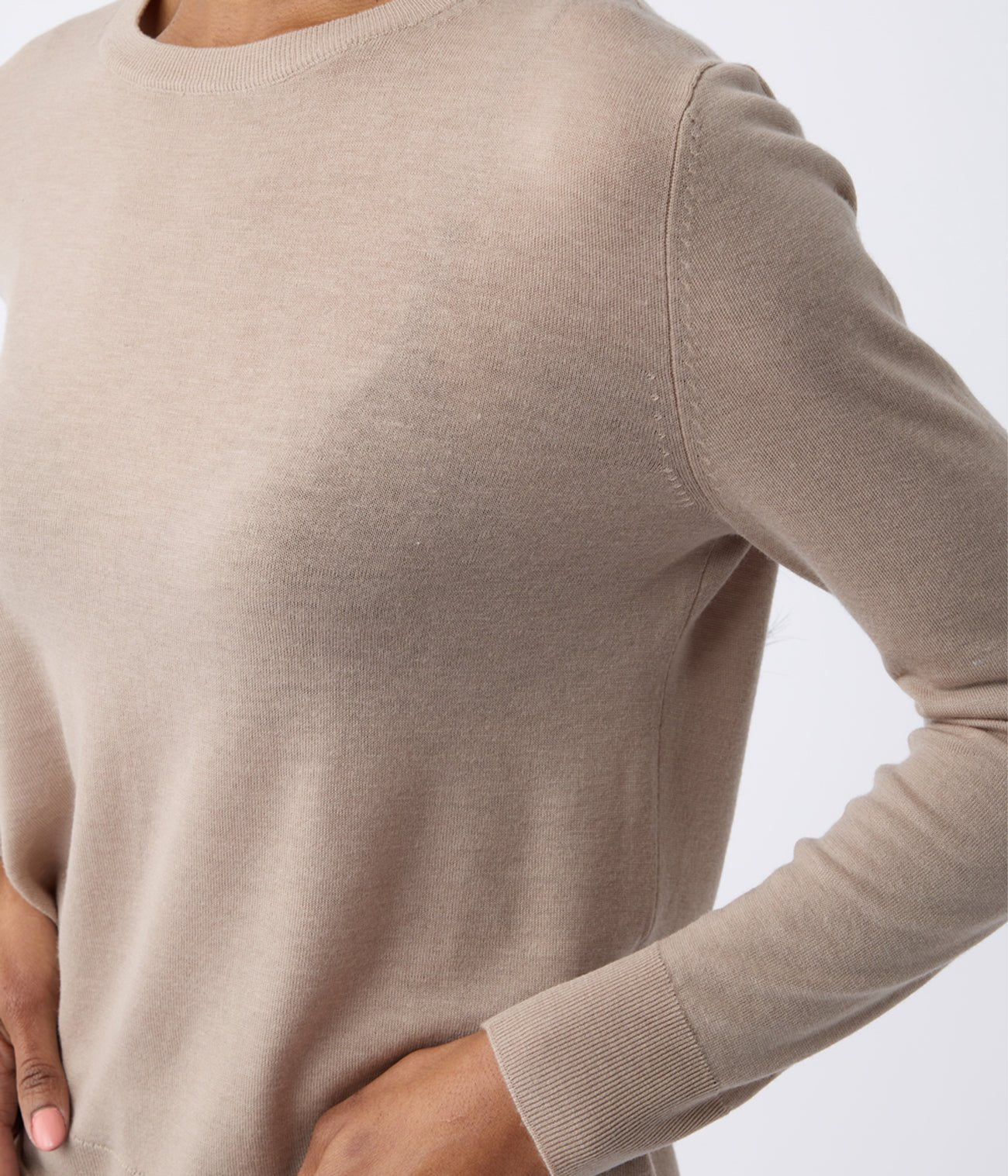 A person wears a Women's AirKnit Crewneck Sweater by Cozy Earth, showcasing its light brown color, long sleeves, texture, and fit with hands on hips against a neutral background. |Color:Taupe