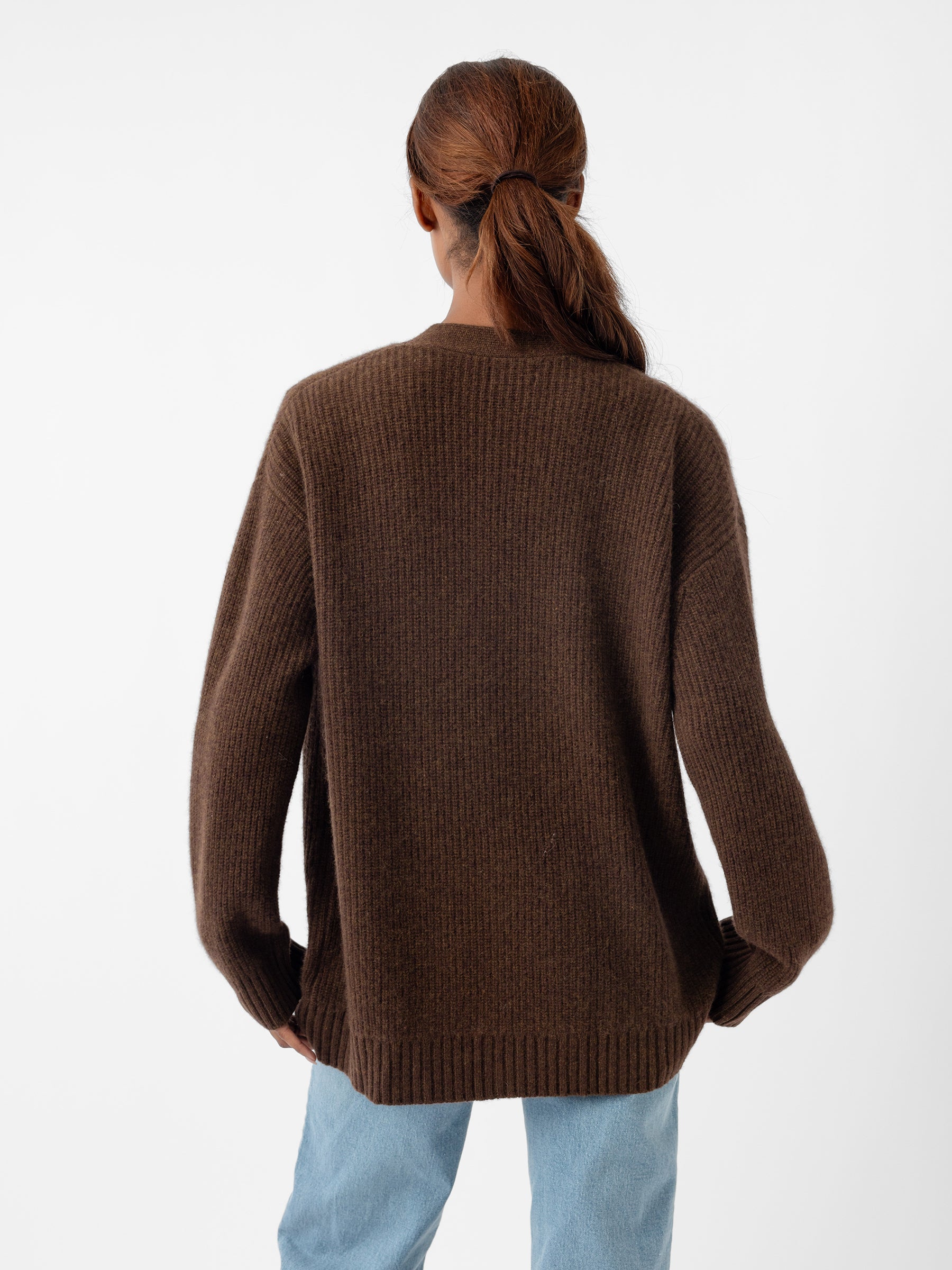 Rear view of a person with brown hair tied in a ponytail, wearing the Cozy Earth Oversized Sunday Cashmere Cardigan and light blue jeans, standing against a plain white background. |Color:Tobacco