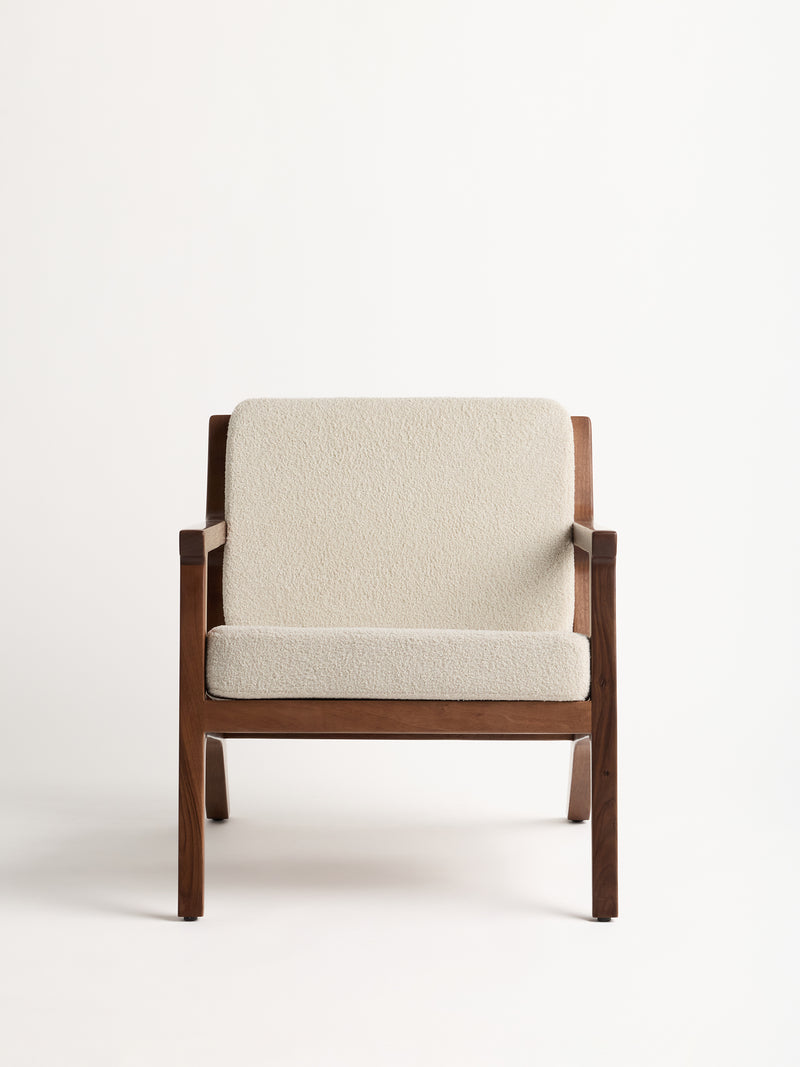 The Coronado Lounge Chair by Cozy Earth is a minimalist wooden armchair with cream-colored upholstery, showcasing a simple and elegant design against a plain white background.