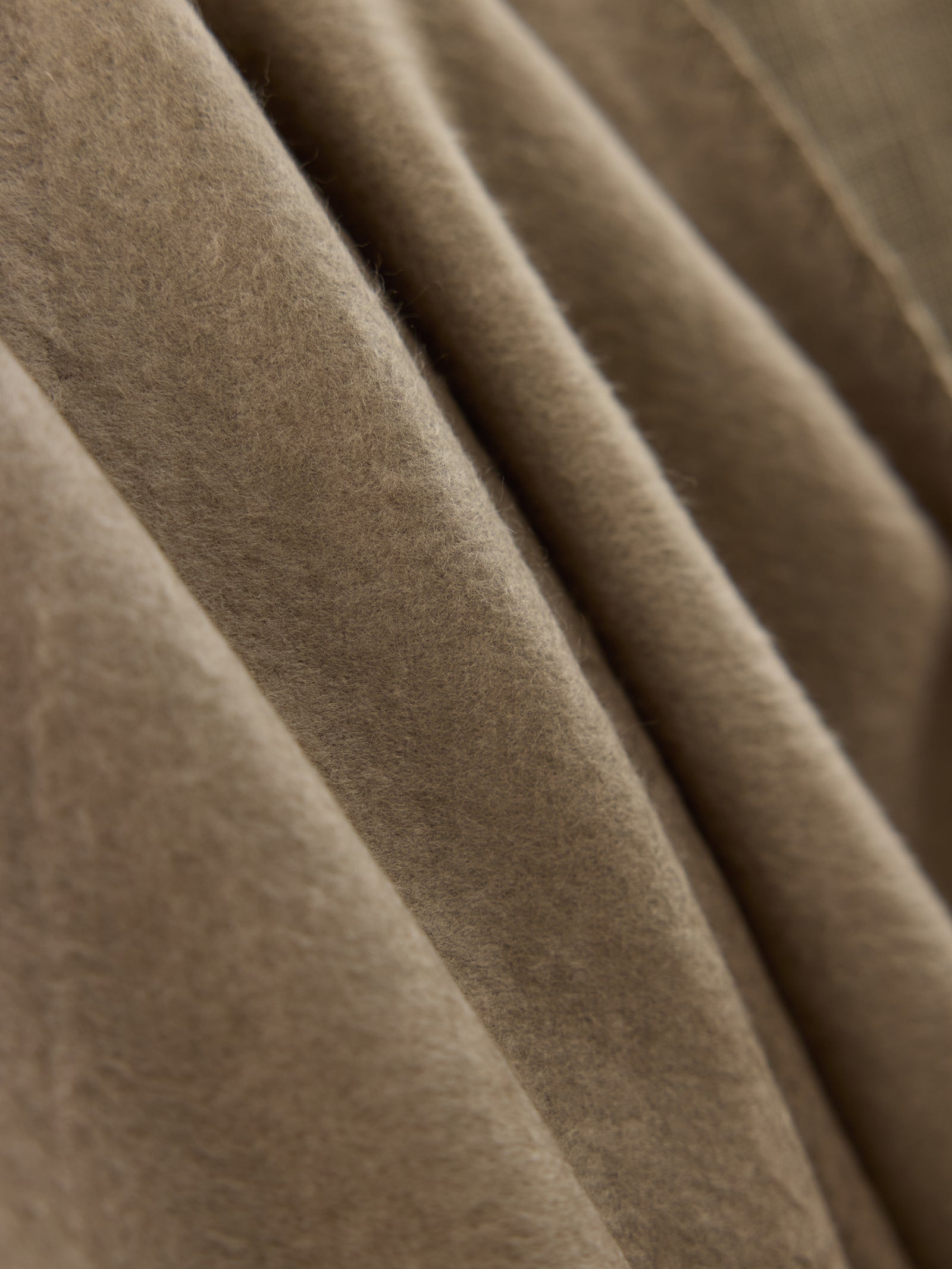 A close-up image of the Bamboo Tassel Throw by Cozy Earth reveals its beige, soft, fuzzy texture. The throw appears to be folded, displaying gentle, flowing creases and shadows. 