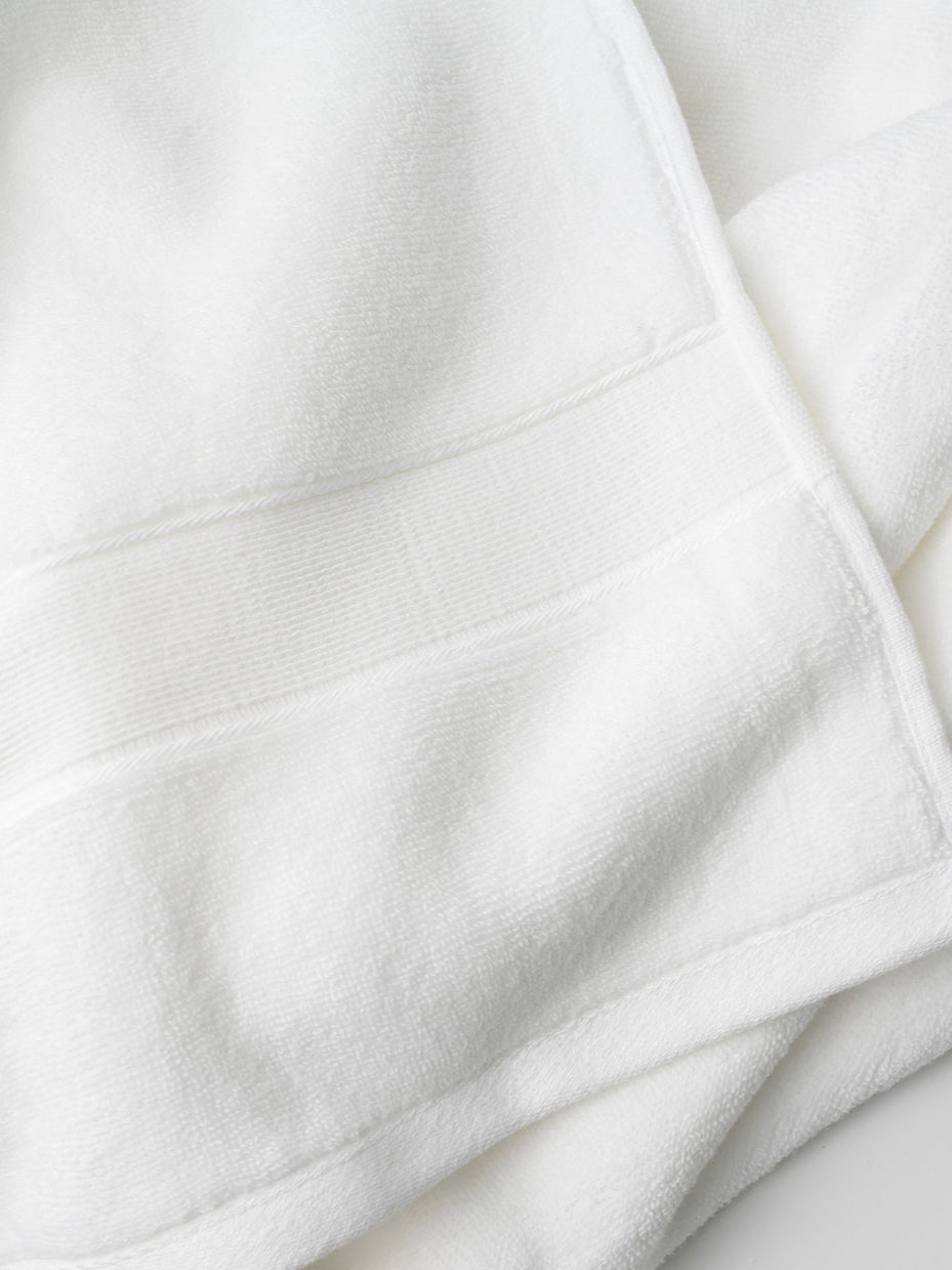 A close-up of a Luxe Bath Towel by Cozy Earth in light blue highlights its textured, soft, and absorbent fabric with detailed stitching and a neatly folded corner.|Color:Tide