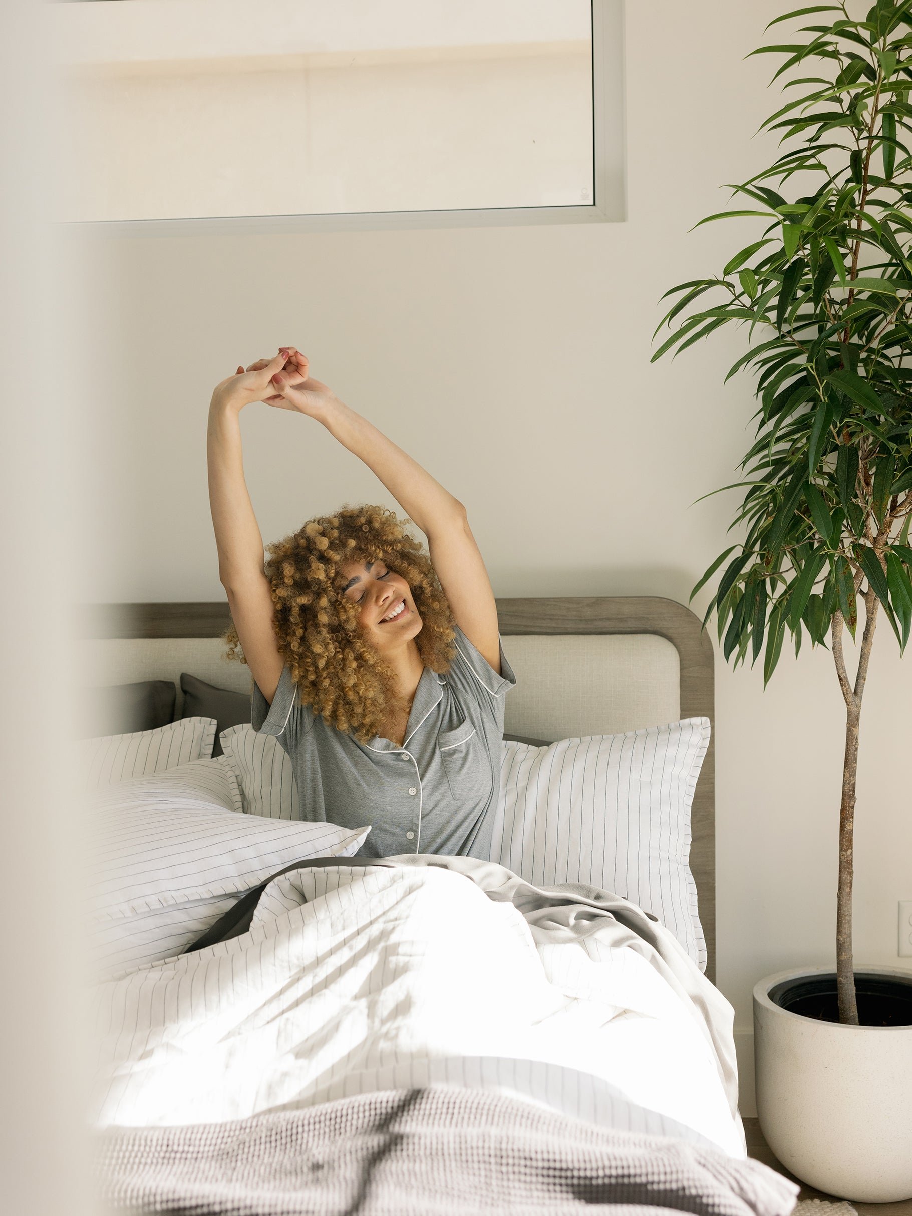 Woman sitting in bed with charcoal pencil stripe shams and quilt 