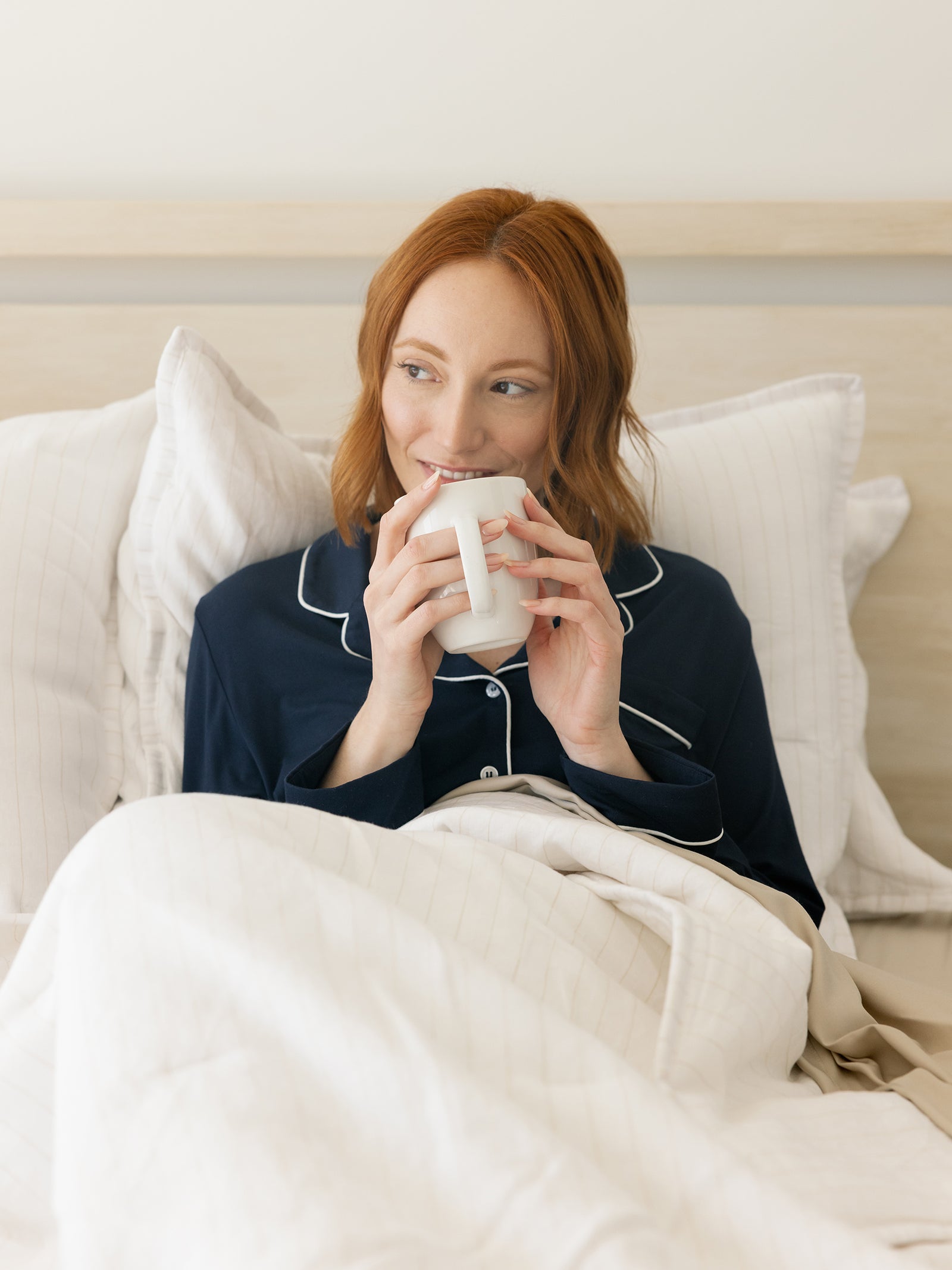 Woman sitting in bed with coffee wrapped in flax pencil stripe quilt 