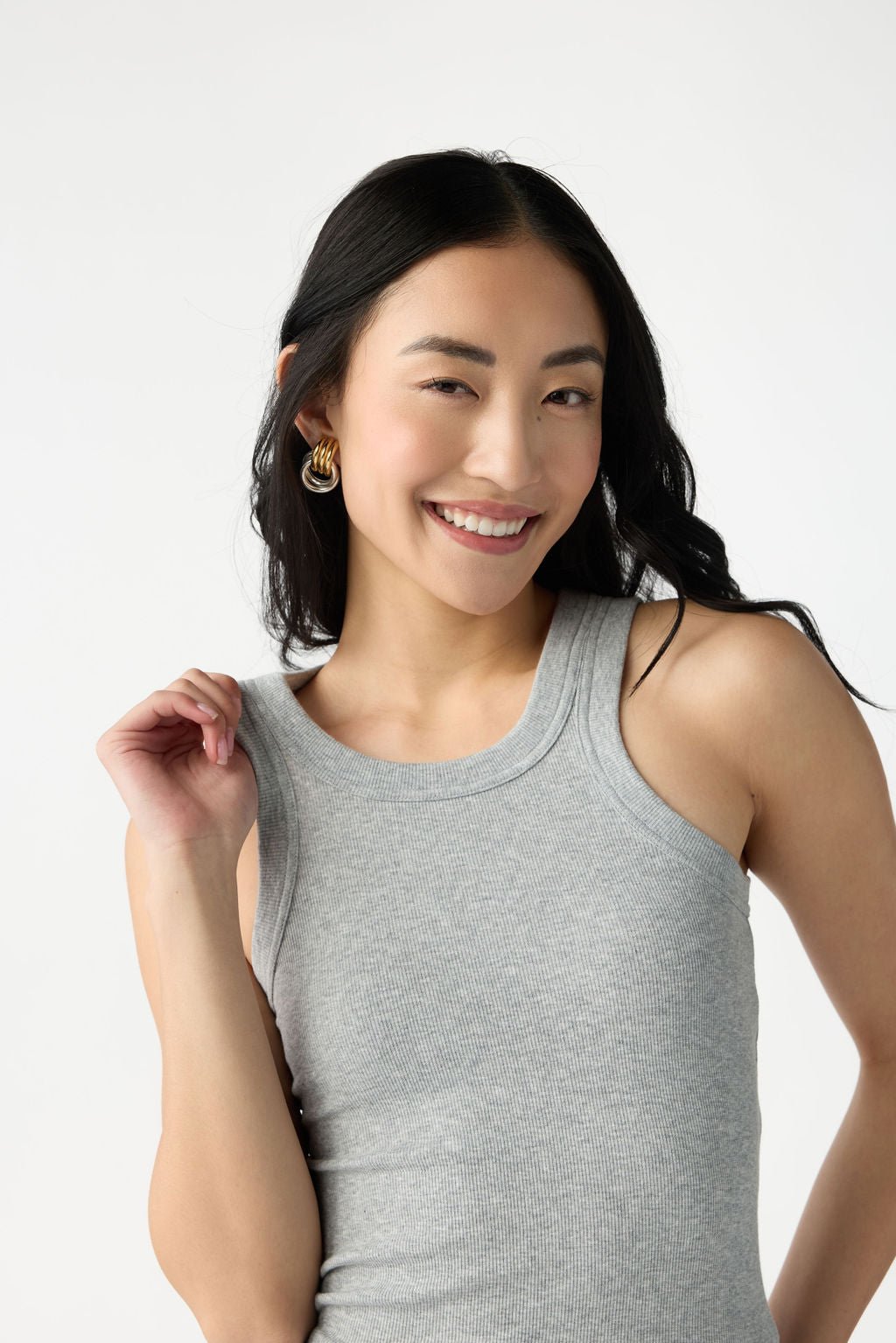 A dark haired woman wears Cozy Earth Women's Fine Ribbed Tank in Heather Grey. She is pictured from the waist up and stands in front of a white background. 