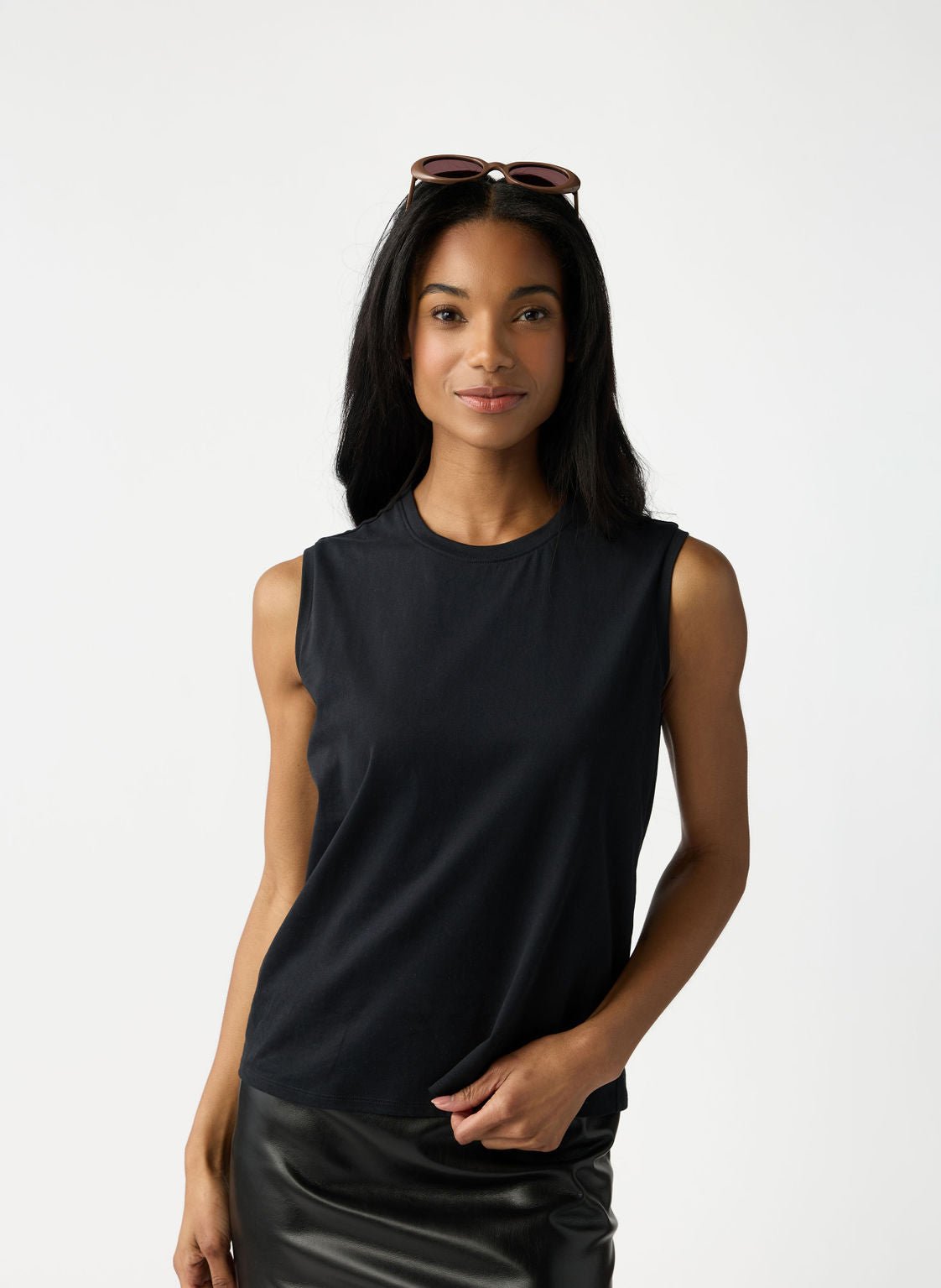 A woman with dark hair and sunglasses on her head wears Cozy Earth Women's All Day Sleeveless Tee in Jet Black. She's shown from the hips up in front of a white background. |Color:Jet Black