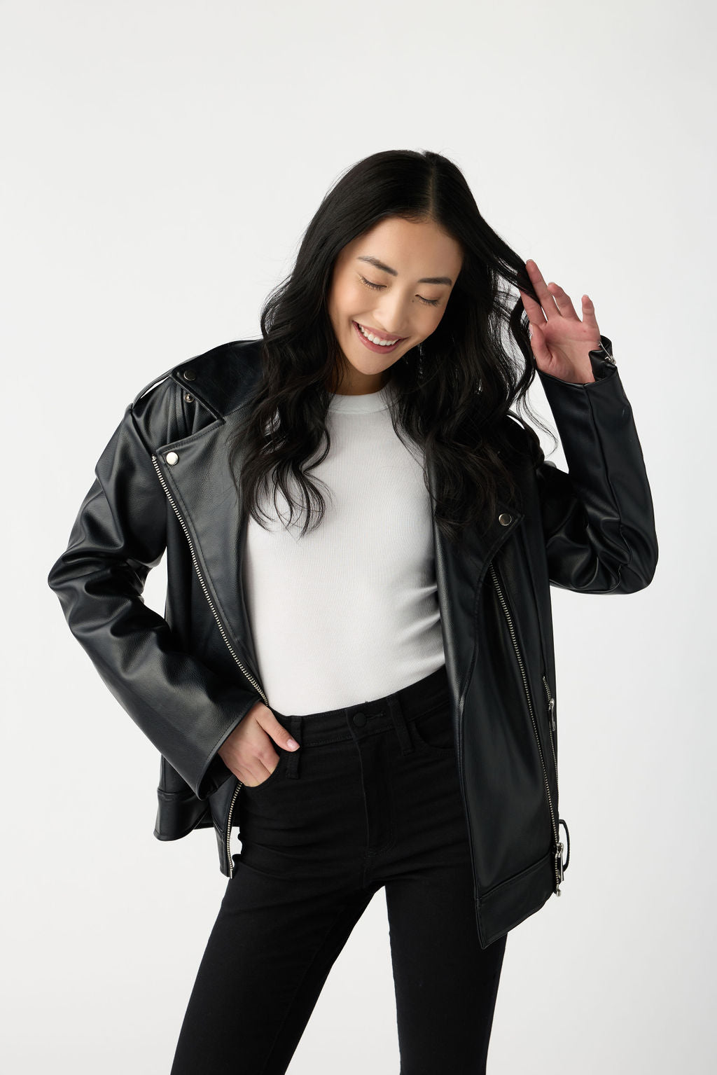 A dark haired woman wears Cozy Earth Women's Fine Ribbed Tee in White under a black leather jacket. She is wearing black pants and stands in front of a white background. 