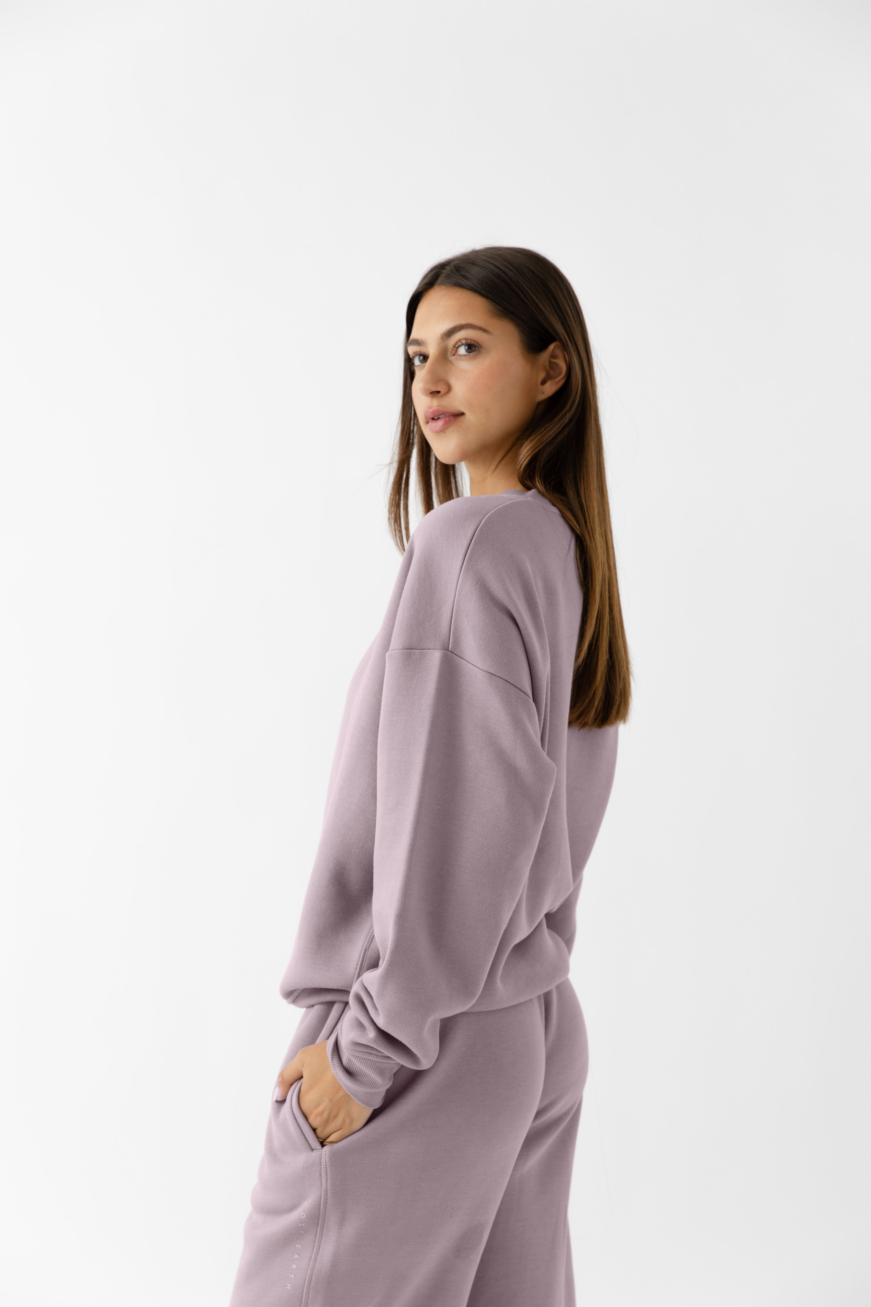 Dusty Orchid CityScape Pullover Crew. The Pullover is being worn by a female model. Accompanying city scape clothing is being worn to complete the look of the outfit. The photo was taken with a white background. |Color:Dusty Orchid