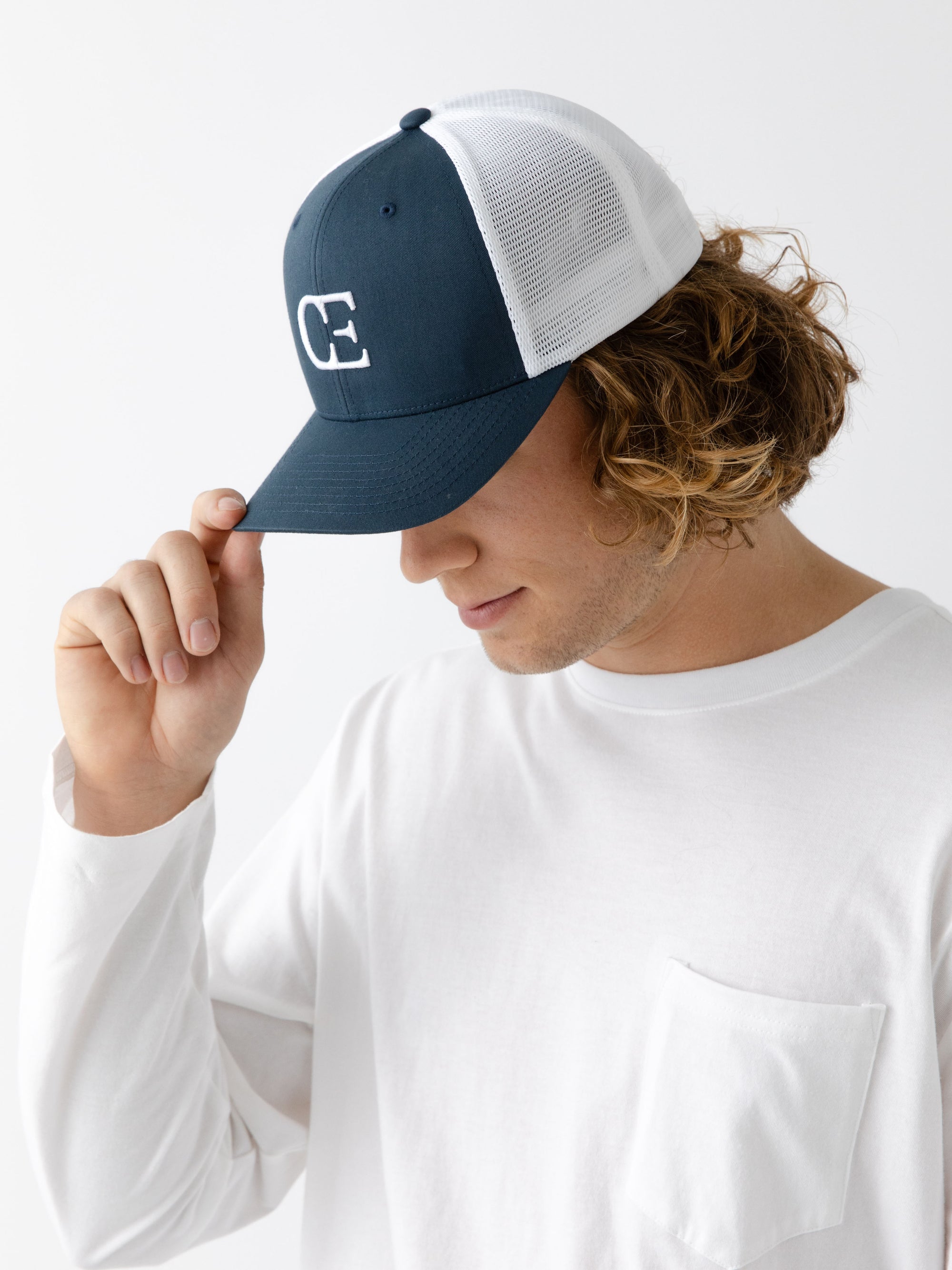 Man wearing a Navy and white cap with a CE logo on a light gray background 