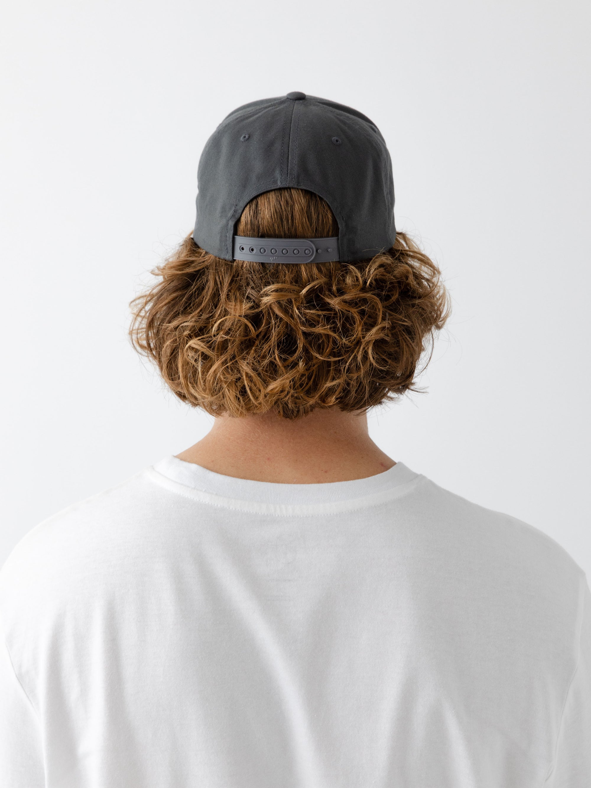 A man wearing a grey cap facing backwards on a white background 